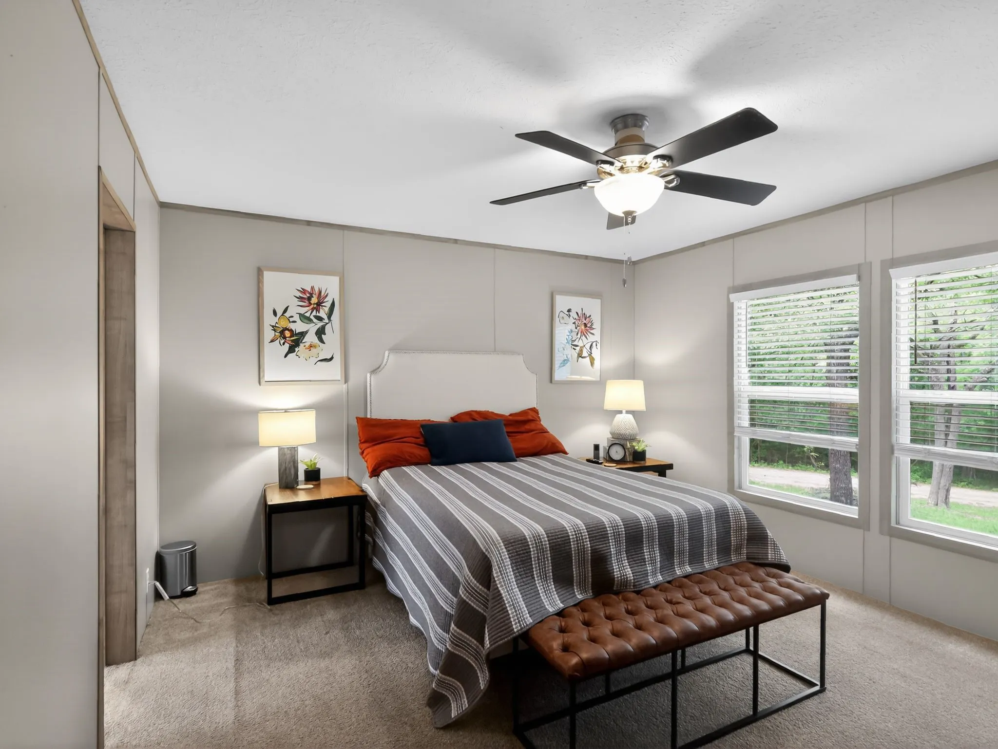 Carpeted interior room featuring light gray walls, multiple windows with blinds, a ceiling fan with integrated lighting, and a recessed doorway