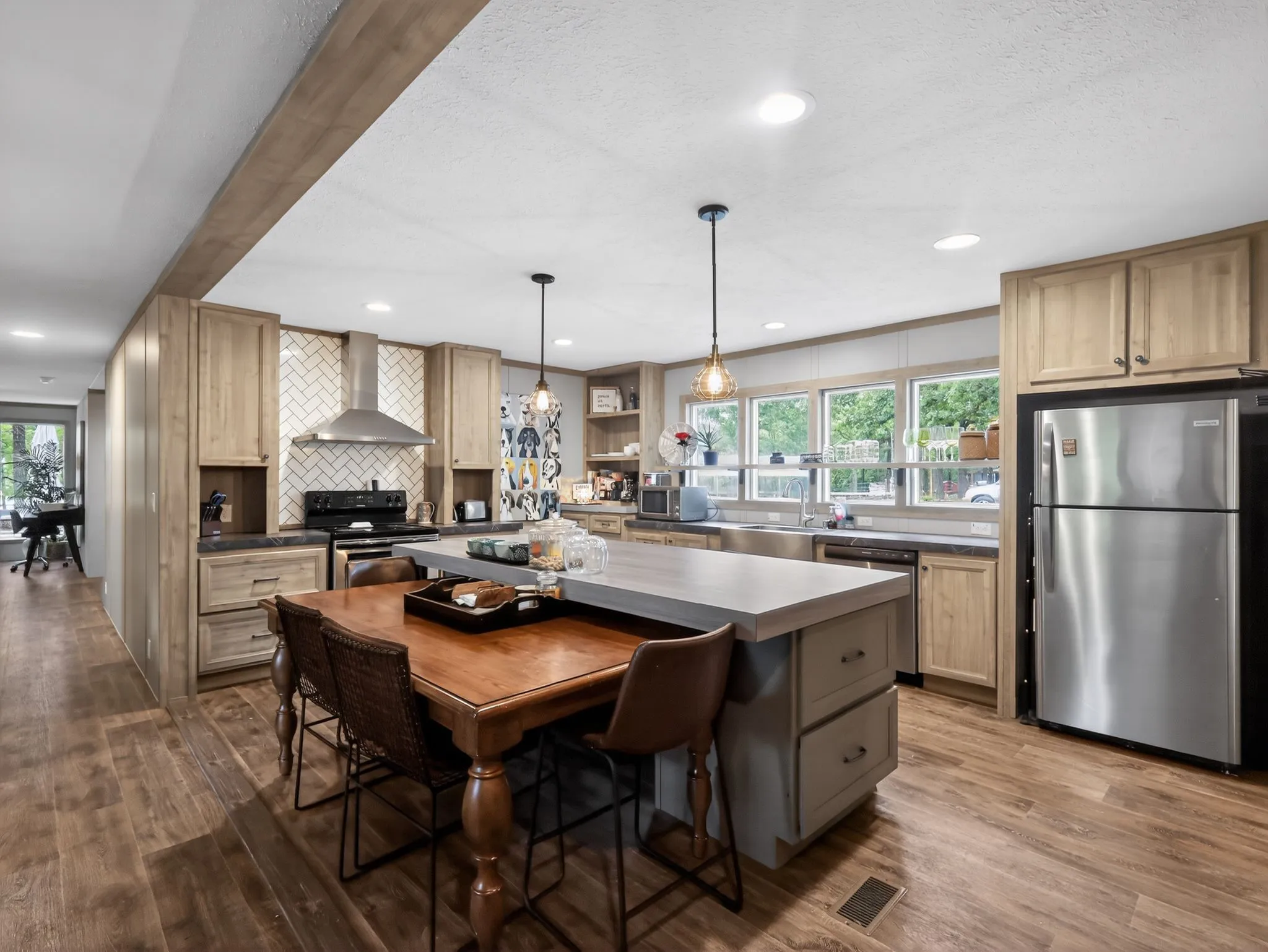 Spacious kitchen featuring wood-finish flooring, light wood cabinetry, stainless steel appliances, a center island with countertop seating, and a herringbone tile backsplash