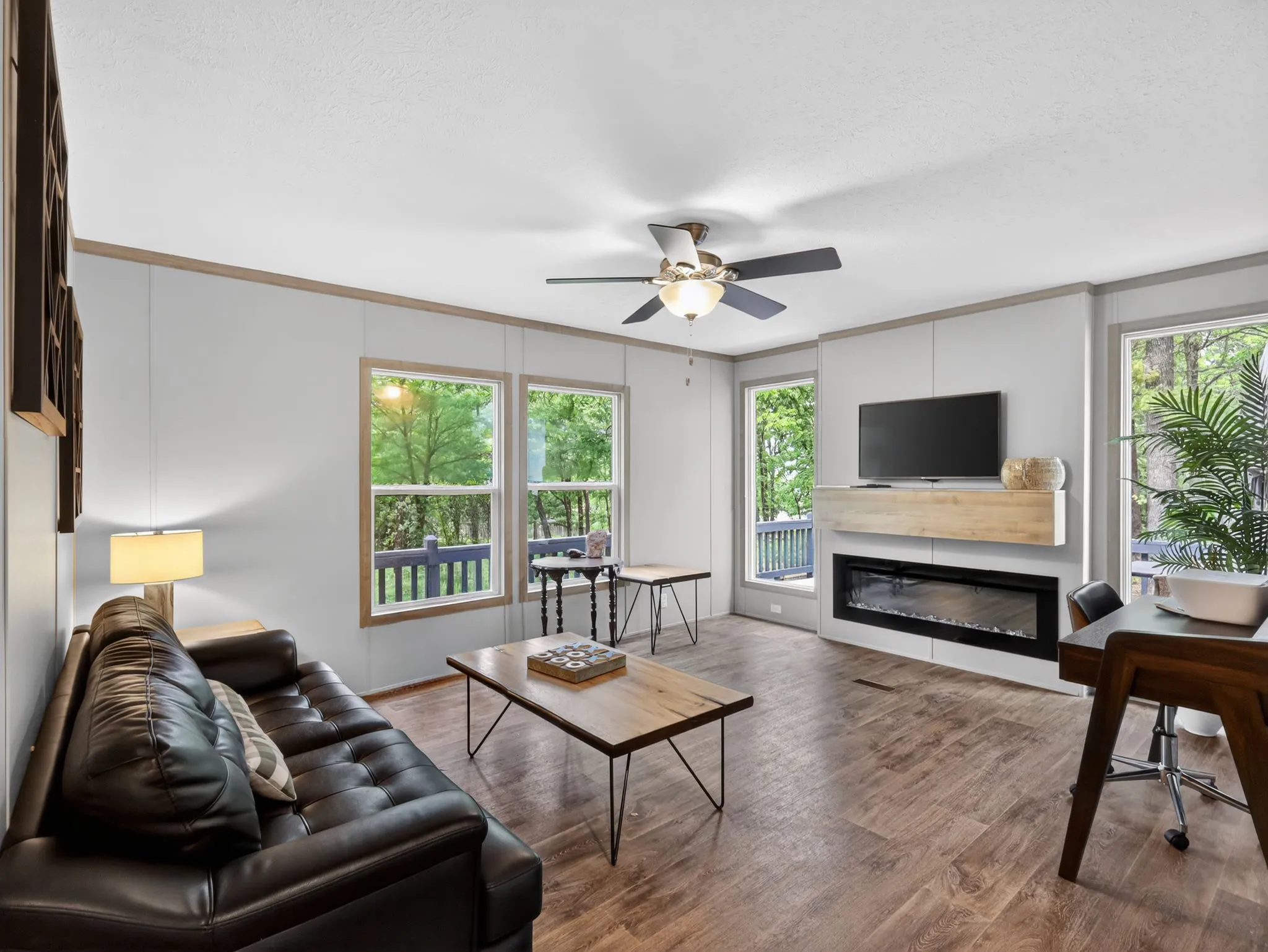Expansive living room featuring wood-finish flooring, a contemporary fireplace with a built-in wooden mantel, and multiple large windows