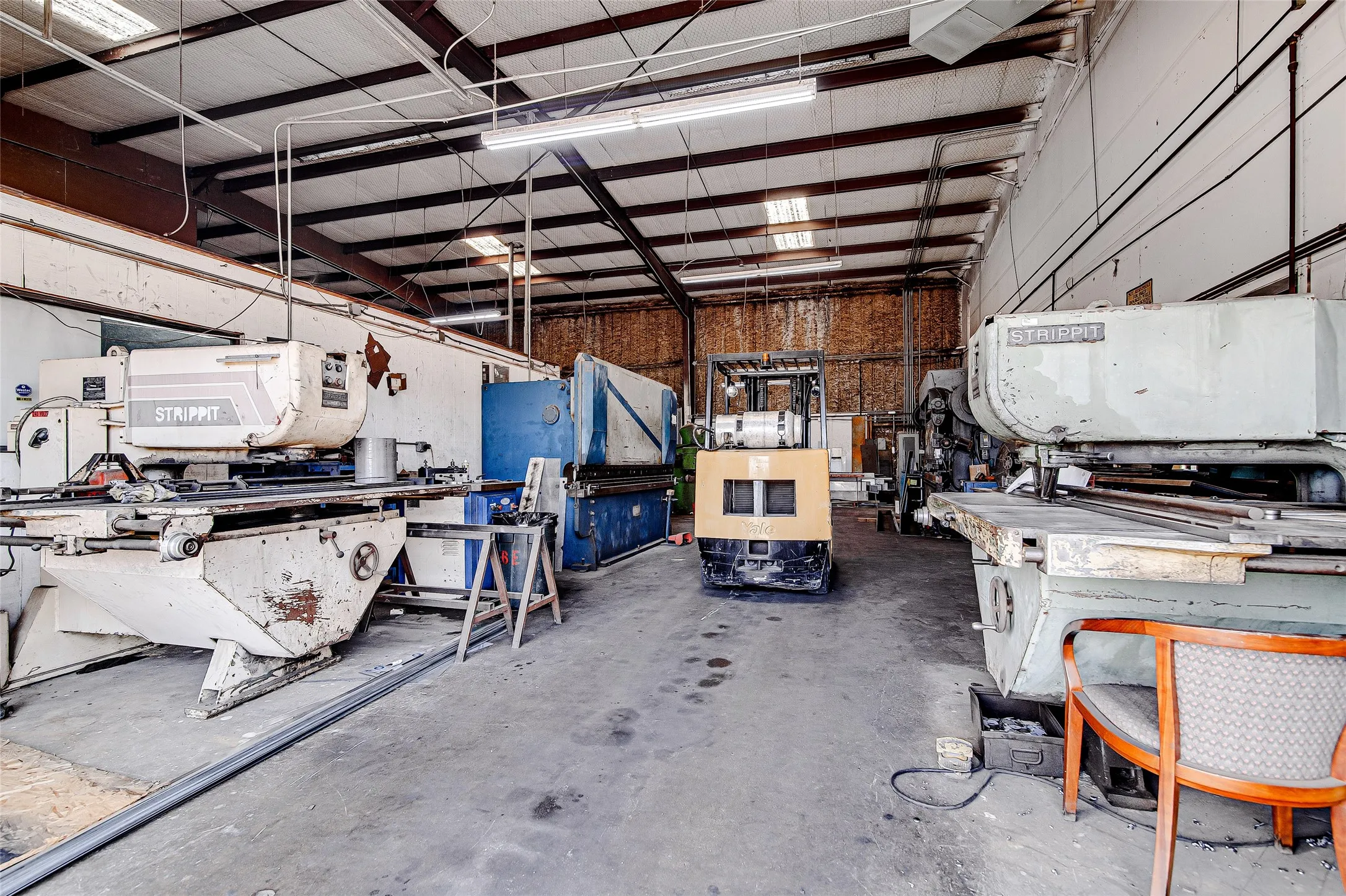 Industrial warehouse space featuring exposed metal truss ceiling, concrete flooring, and ample overhead lighting