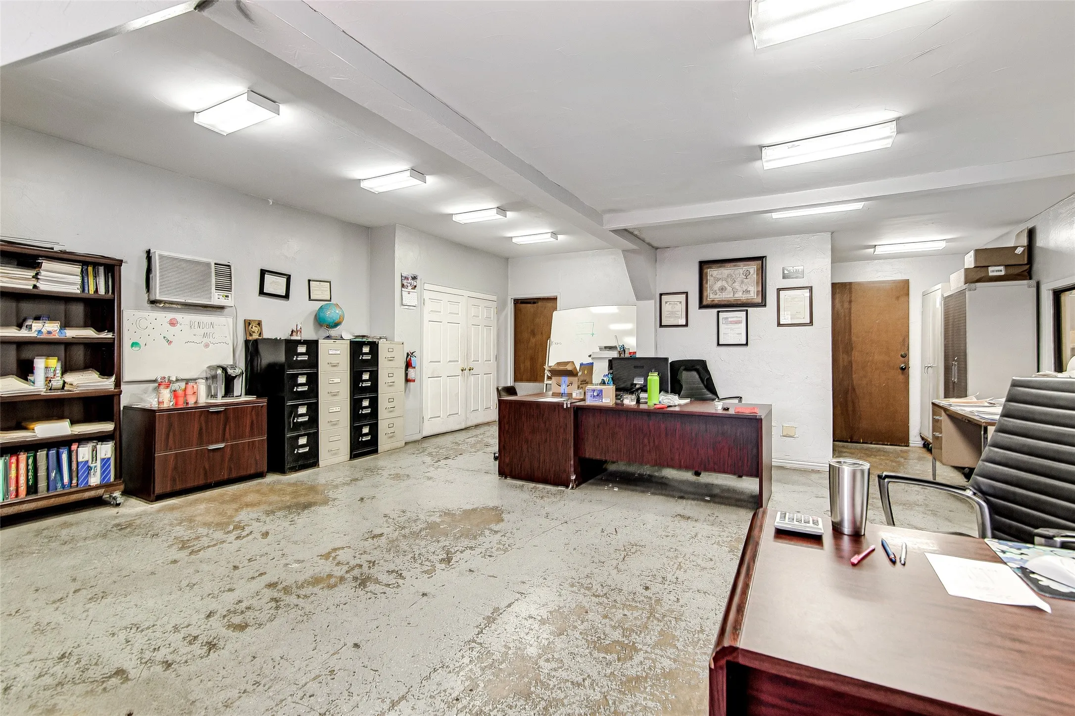Spacious commercial interior featuring concrete flooring, white walls, and multiple ceiling-mounted light fixtures