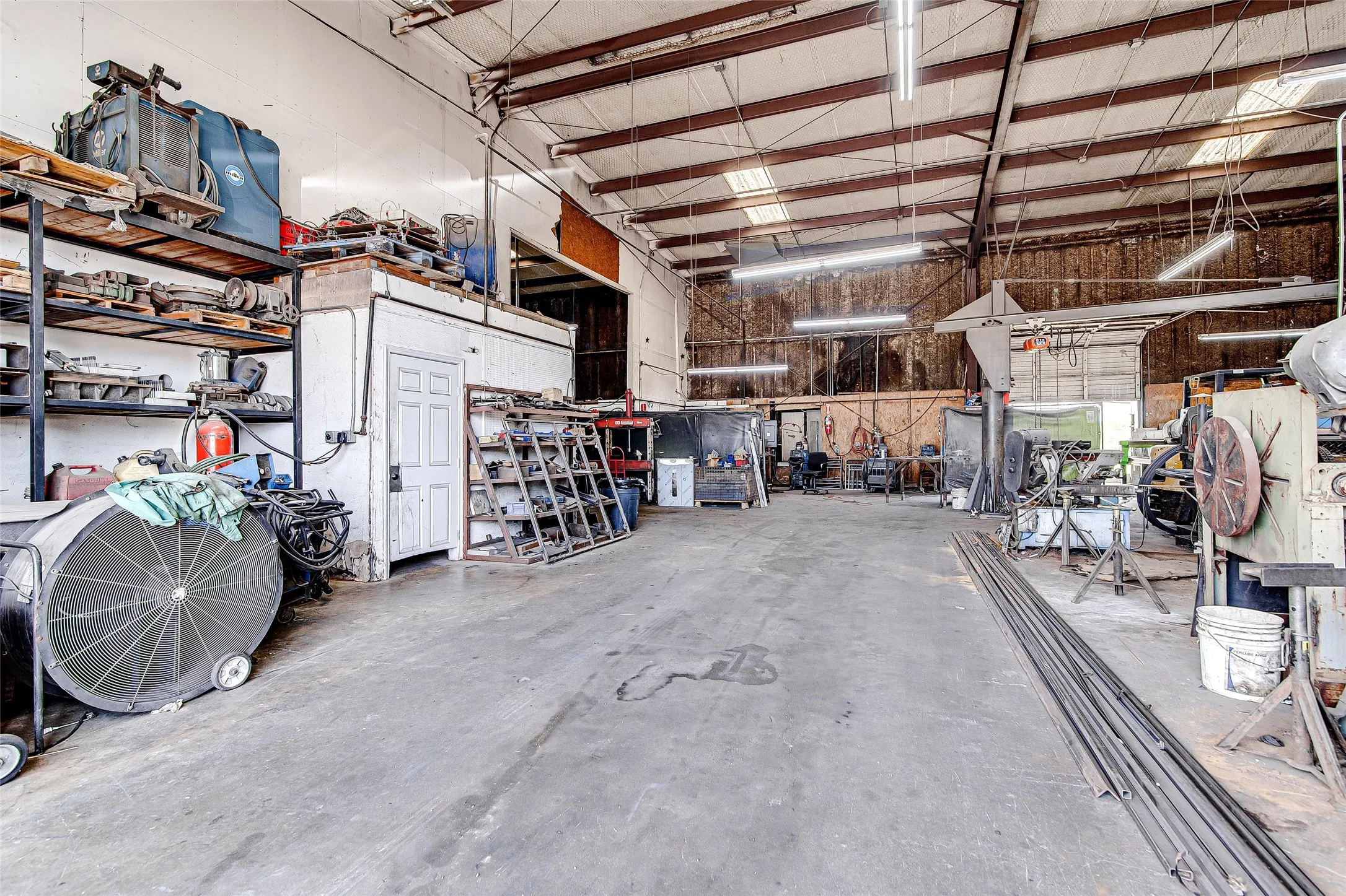 Spacious industrial interior featuring a concrete floor, exposed structural beams, high ceilings, and fluorescent lighting