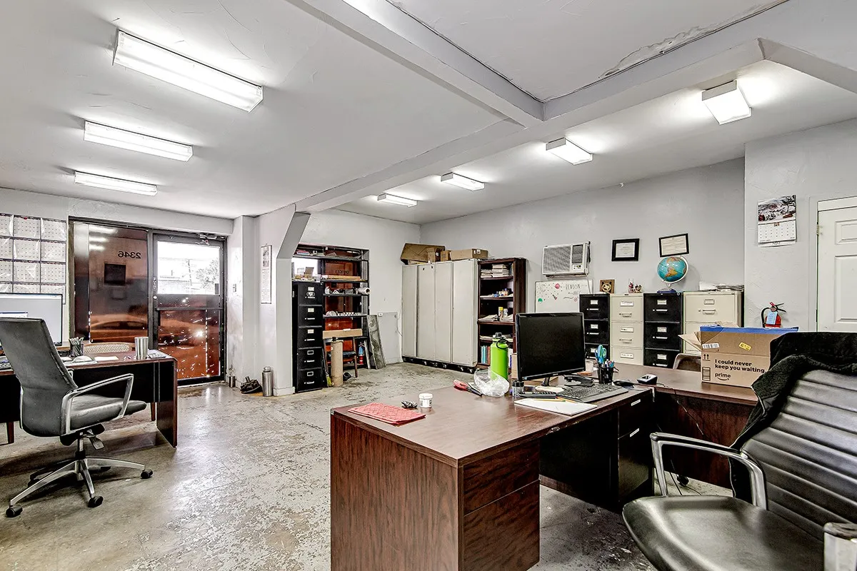 Spacious interior featuring a glass-paneled entry door, block glass window, concrete flooring, and suspended ceiling with fluorescent and square flush mount lighting