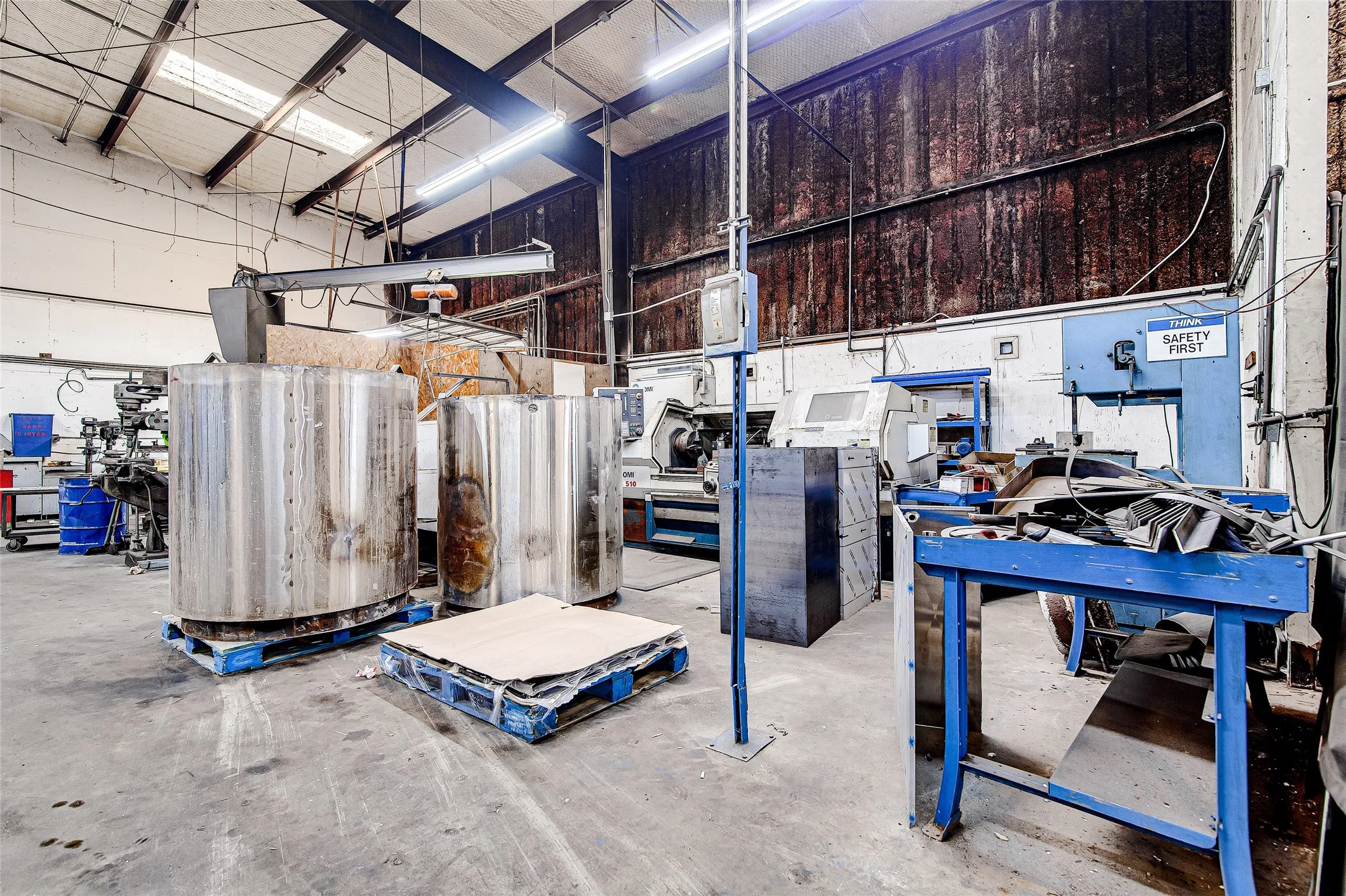 Industrial interior featuring high ceilings with exposed structural beams, fluorescent lighting, and concrete flooring