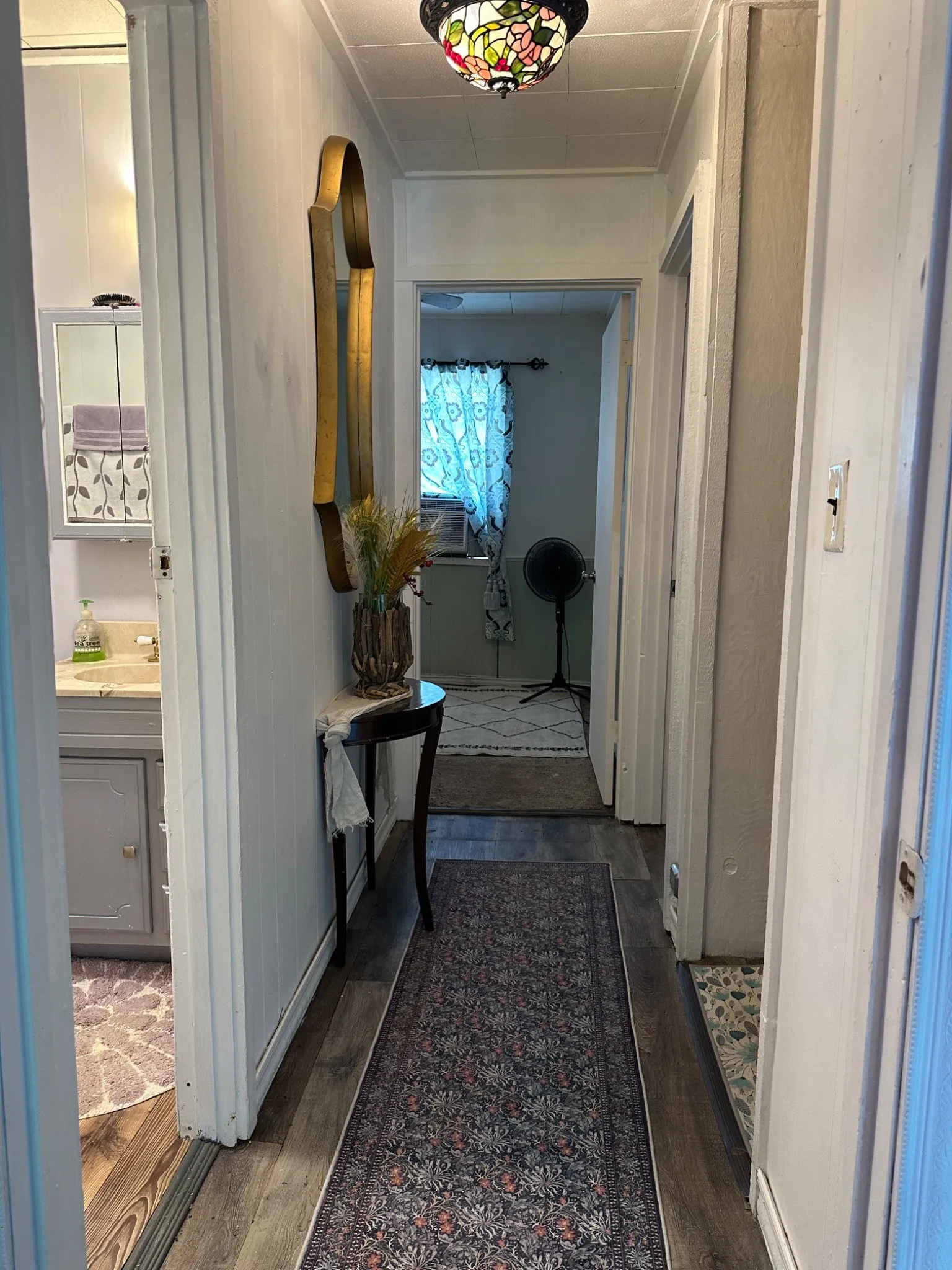 Hallway with wood-finish flooring, a Tiffany-style ceiling light fixture, and white trim