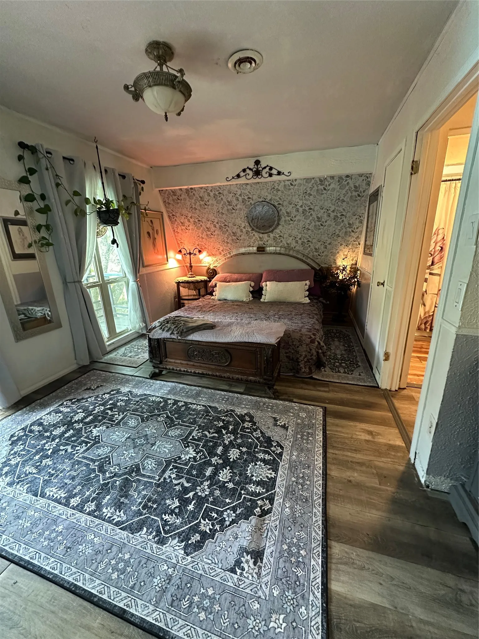 Spacious room featuring wood-finish flooring, an ornate ceiling light fixture, and a decorative wall panel above the bed