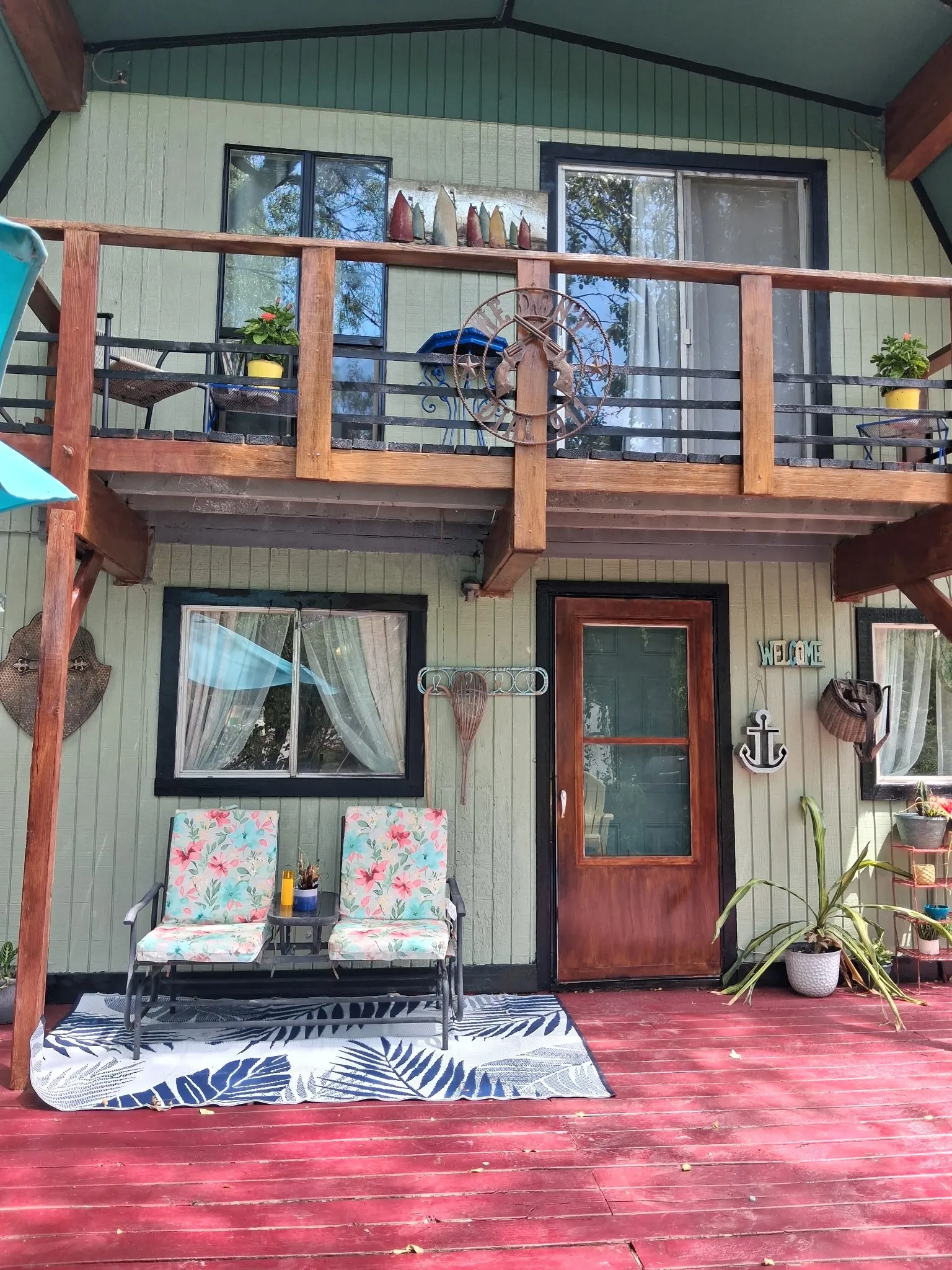 Two-story exterior with a red-stained wood deck, upper-level balcony, and a paneled front door