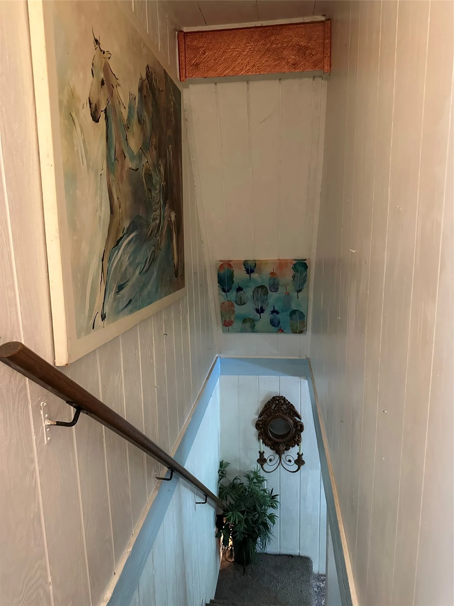 Stairwell featuring vertical paneling, a wood handrail, and sconce lighting