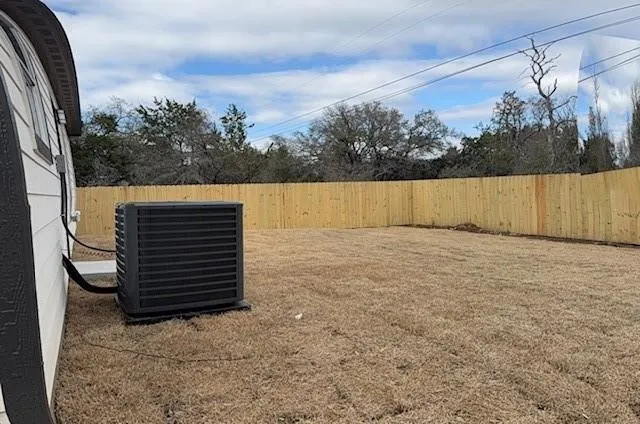 Expansive backyard featuring a newly installed wood privacy fence, a modern outdoor HVAC unit, and a broad grassy area