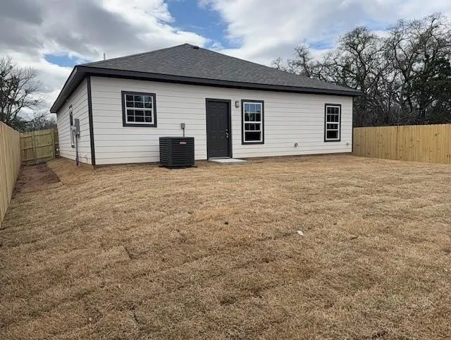 Rear exterior featuring light-colored horizontal siding with black trim, dark shingle roof, and a dark entry door