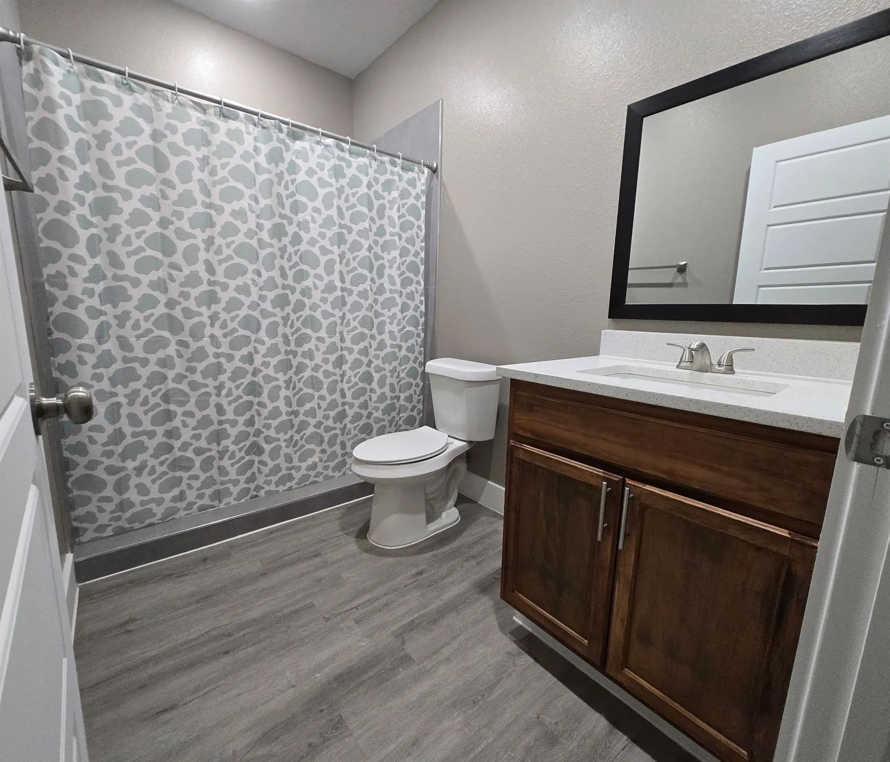 Bathroom featuring a wood-finish vanity with a light-toned countertop, an integrated sink, and a framed mirror