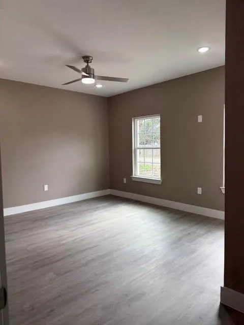 Spacious room featuring wood-finish flooring, a contemporary ceiling fan, recessed lighting, and a double-pane window with a white frame