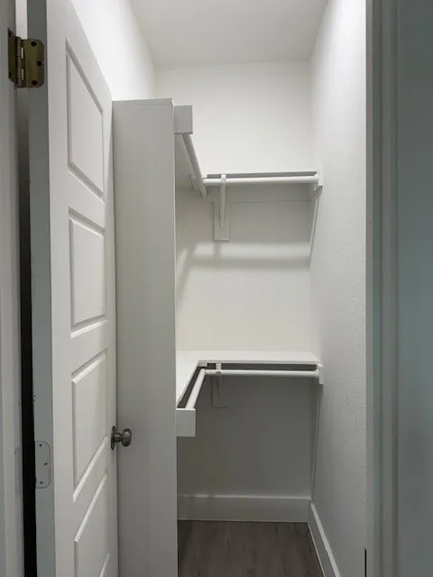 Walk-in closet featuring white walls, shelving, and clothing rods, complemented by wood-finish flooring and white baseboards