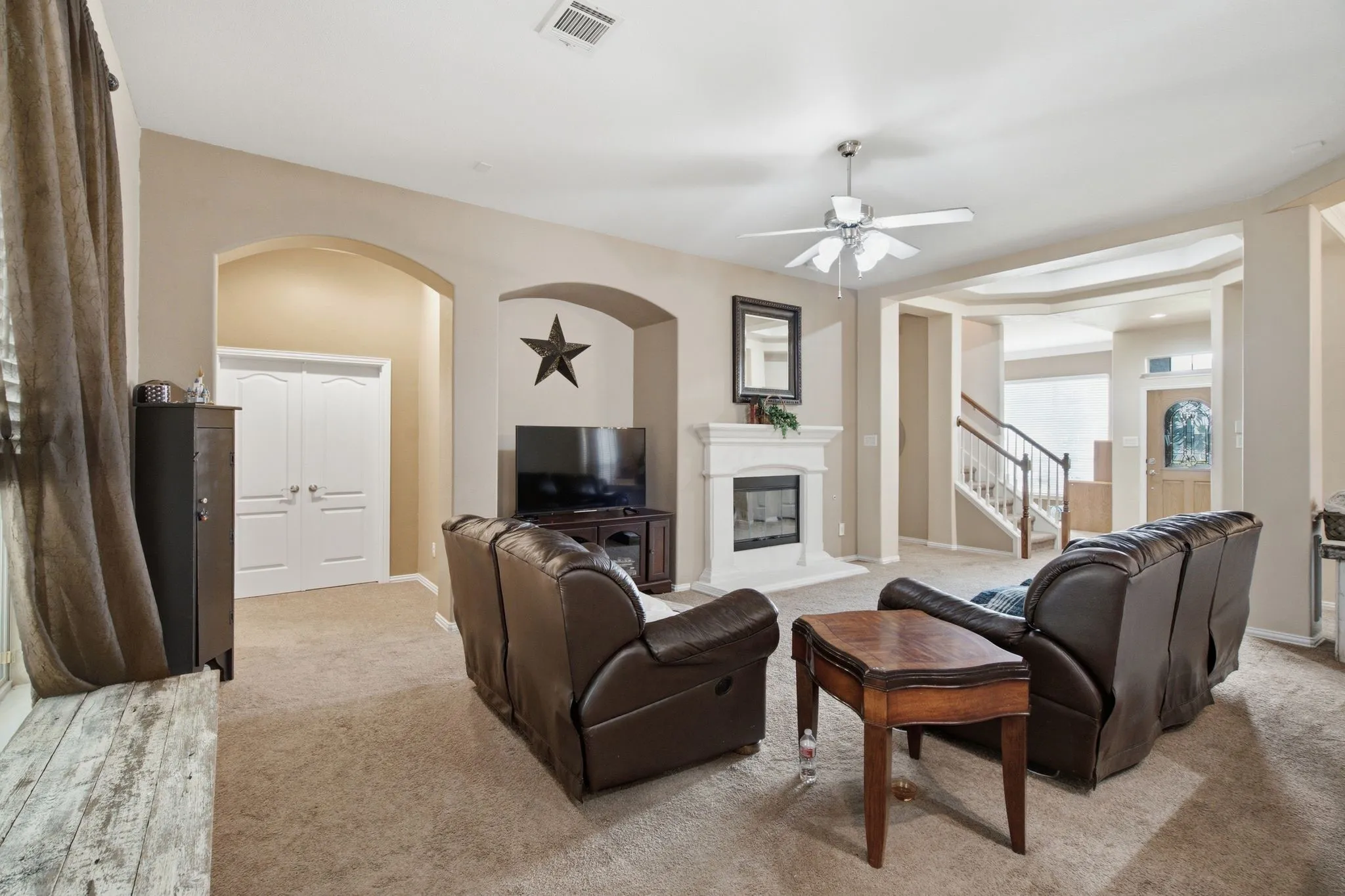 Spacious living area featuring a fireplace with a mantel, a ceiling fan, and carpet flooring