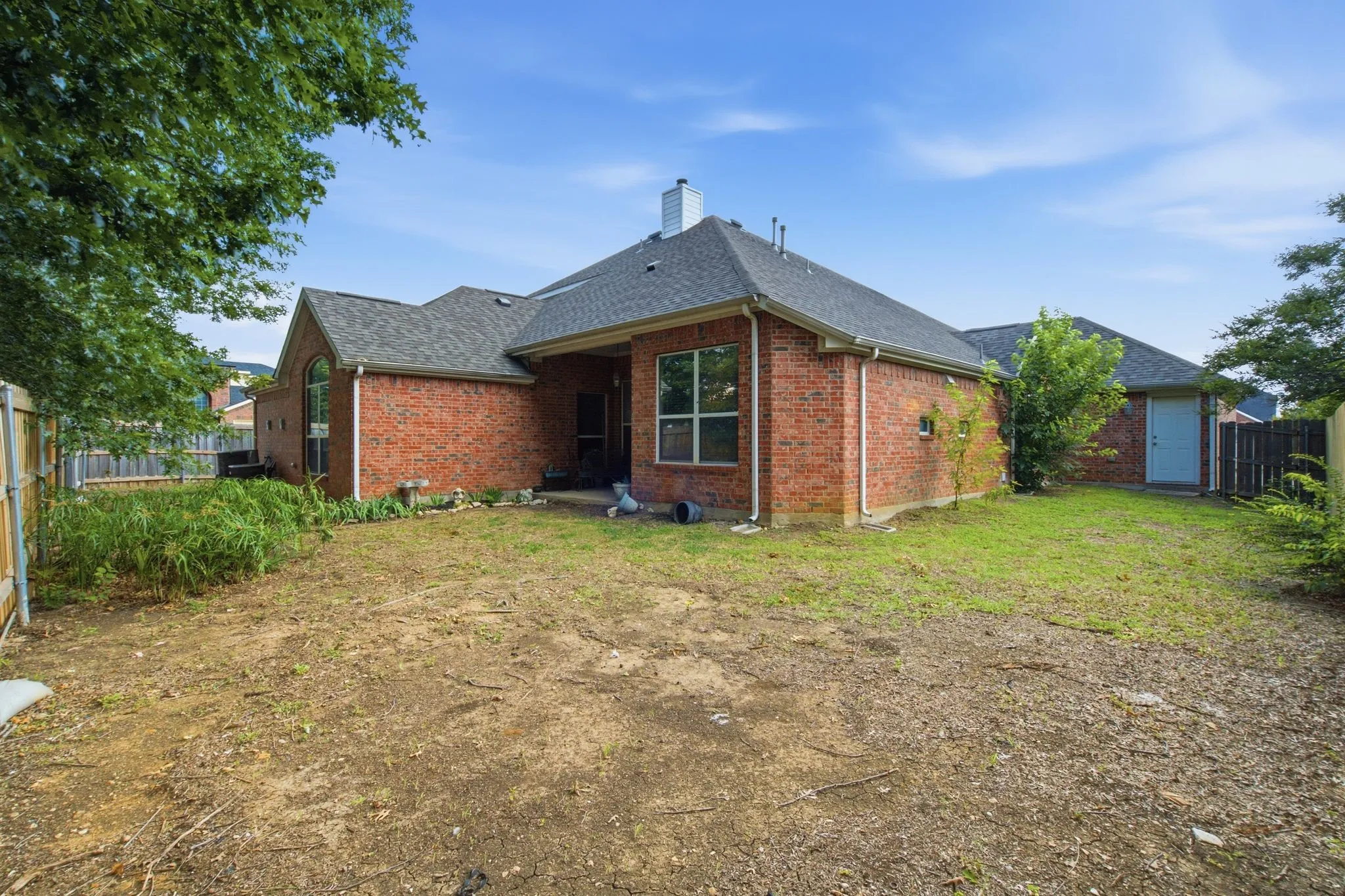 Rear exterior showcasing brick facade, dark shingle roofing, multiple windows, and a partially covered patio area