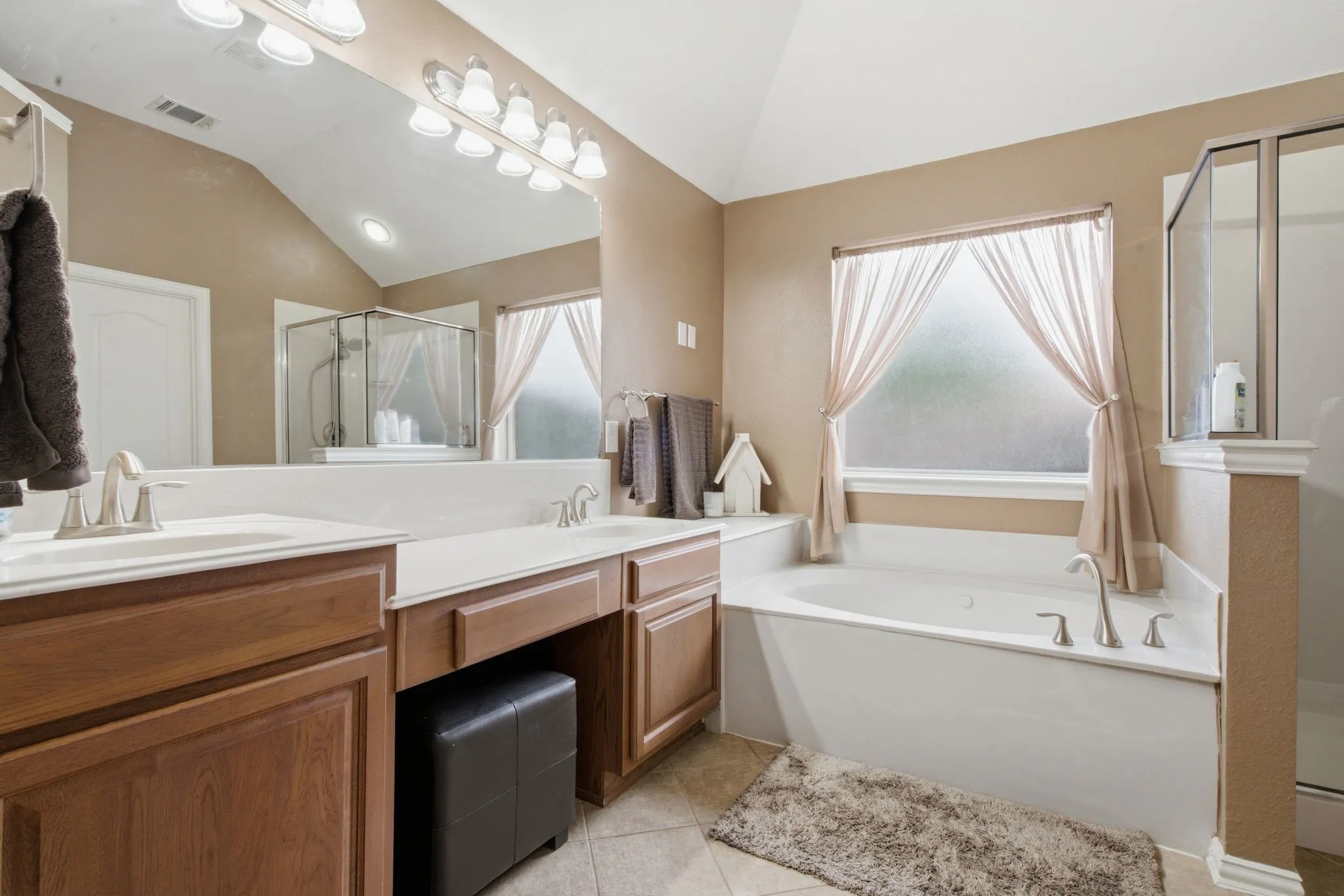 Bathroom featuring a dual vanity with light wood-finish cabinetry, a large mirror, and a built-in tub with a window