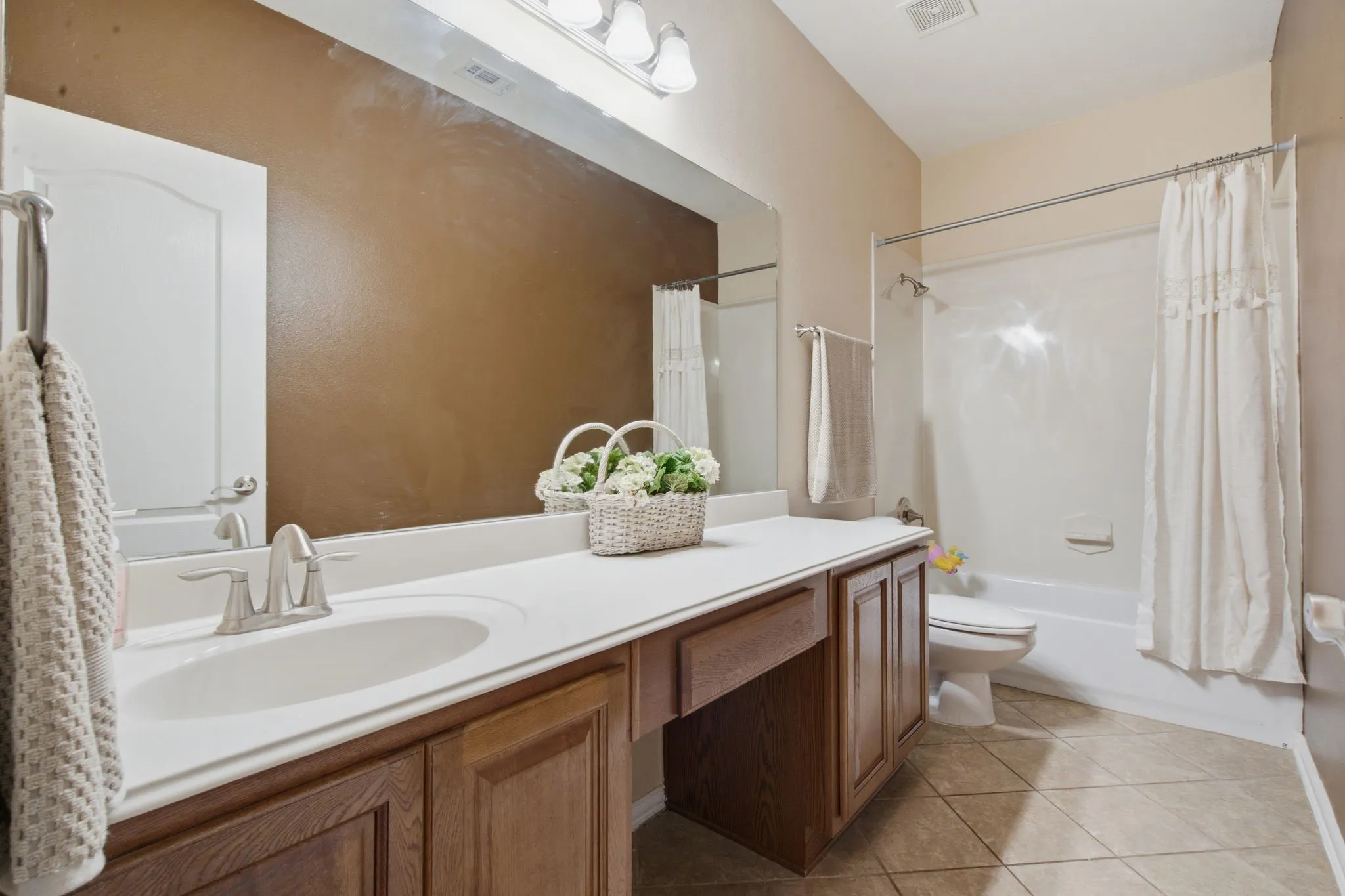 Bathroom featuring a long vanity with dual sinks, wood-finish cabinetry, a white countertop, and a built-in shower/tub combination