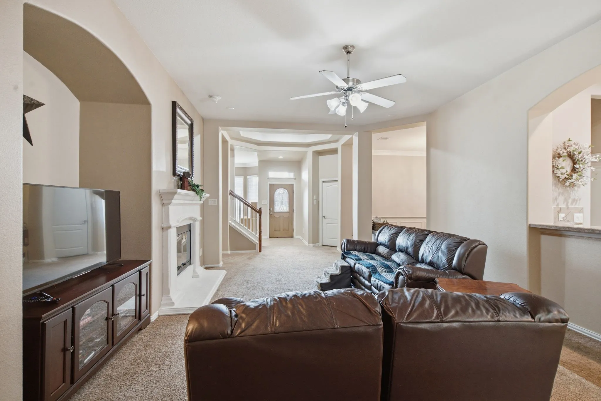 Living area featuring an arched entryway, a fireplace with a white mantel, and carpet flooring