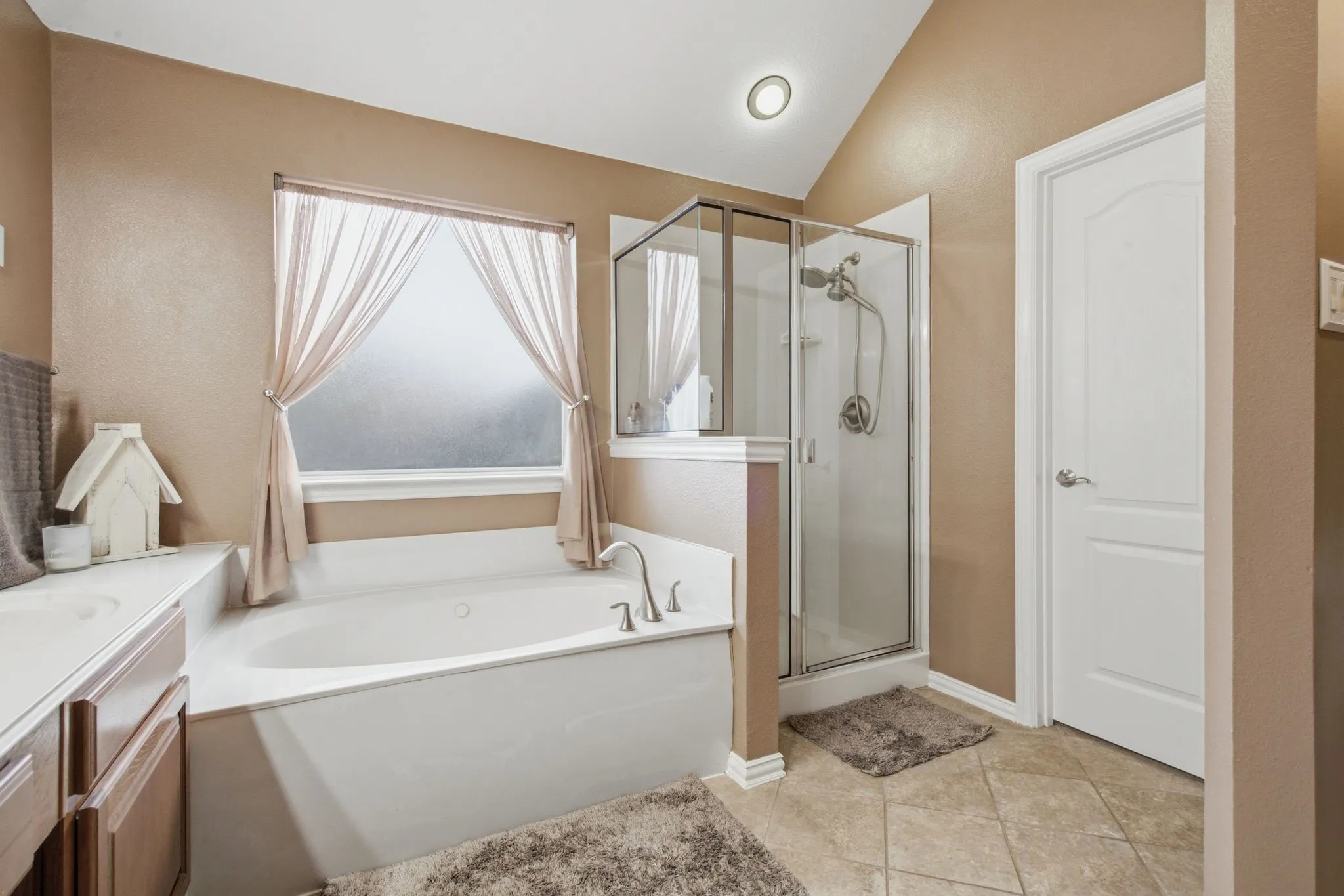 Bathroom featuring a built-in soaking tub, a glass-enclosed shower, a frosted window, tile flooring, and a vaulted ceiling with recessed lighting
