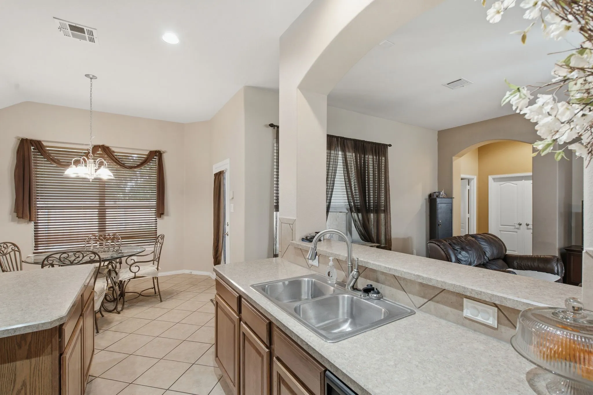 Open-concept kitchen featuring a dual basin stainless steel sink, light-toned countertops, and wood-finish cabinetry