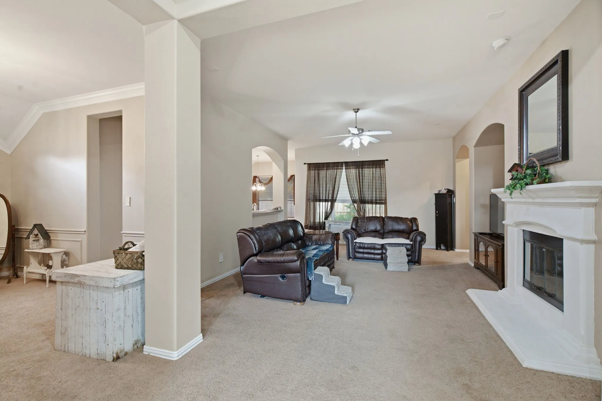 Spacious living area featuring a built-in fireplace with a white mantel, vaulted ceilings, and an overhead ceiling fan
