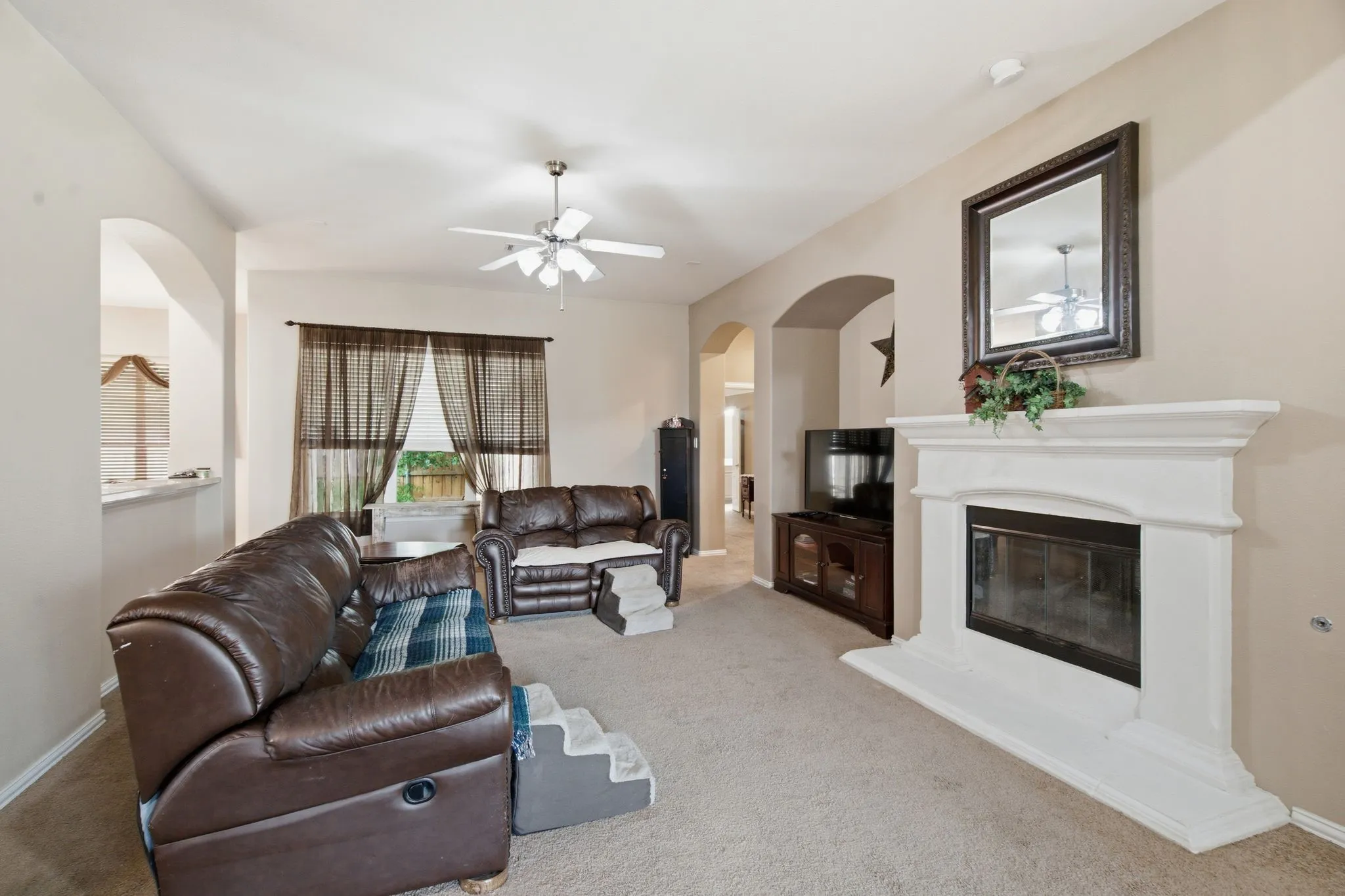 Living area with a built-in fireplace featuring a white mantel, neutral carpeting, and a ceiling fan