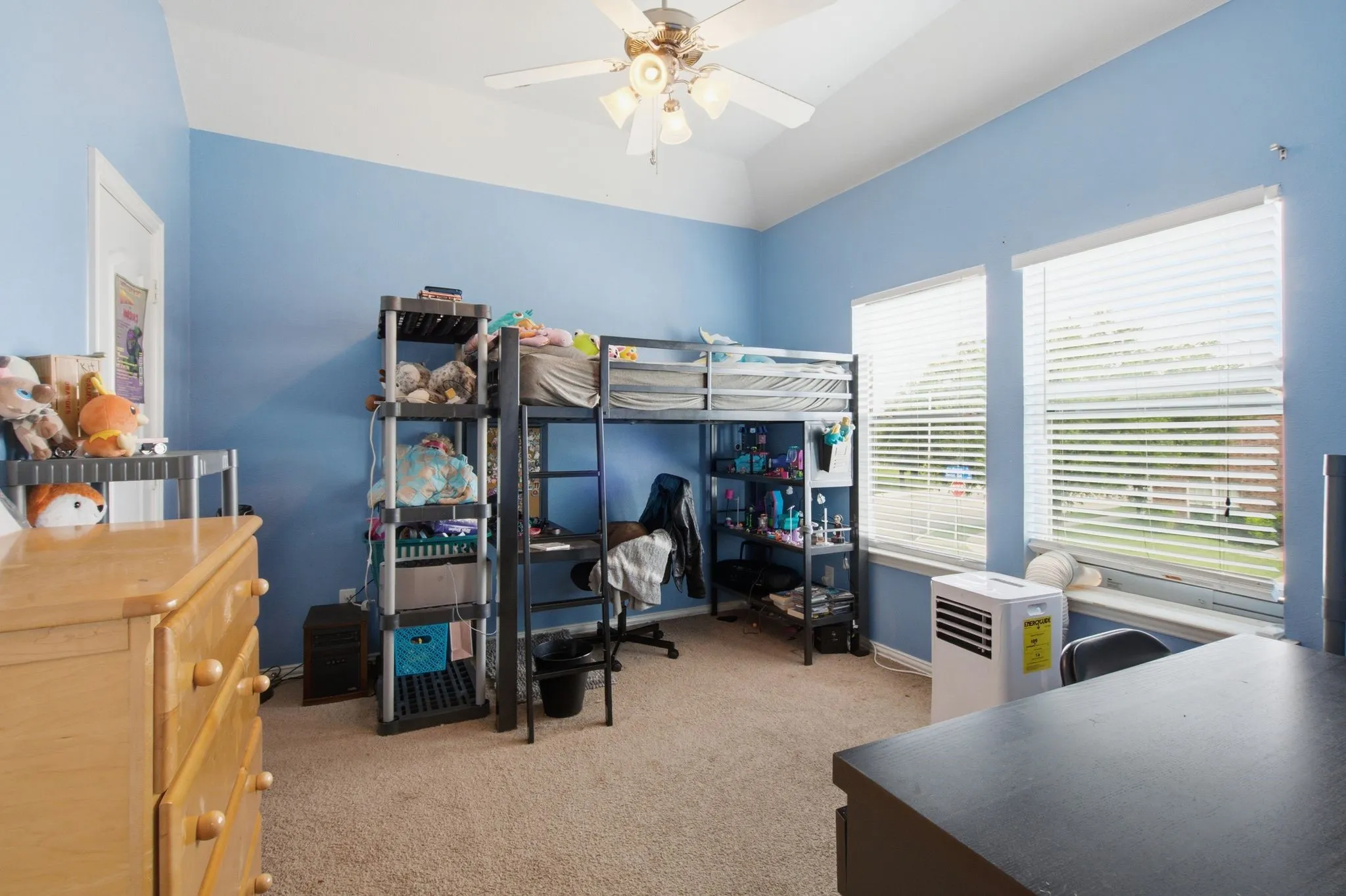 Upstairs bedroom featuring vaulted ceilings, a ceiling fan with integrated lighting, two large windows with blinds, and neutral carpet flooring