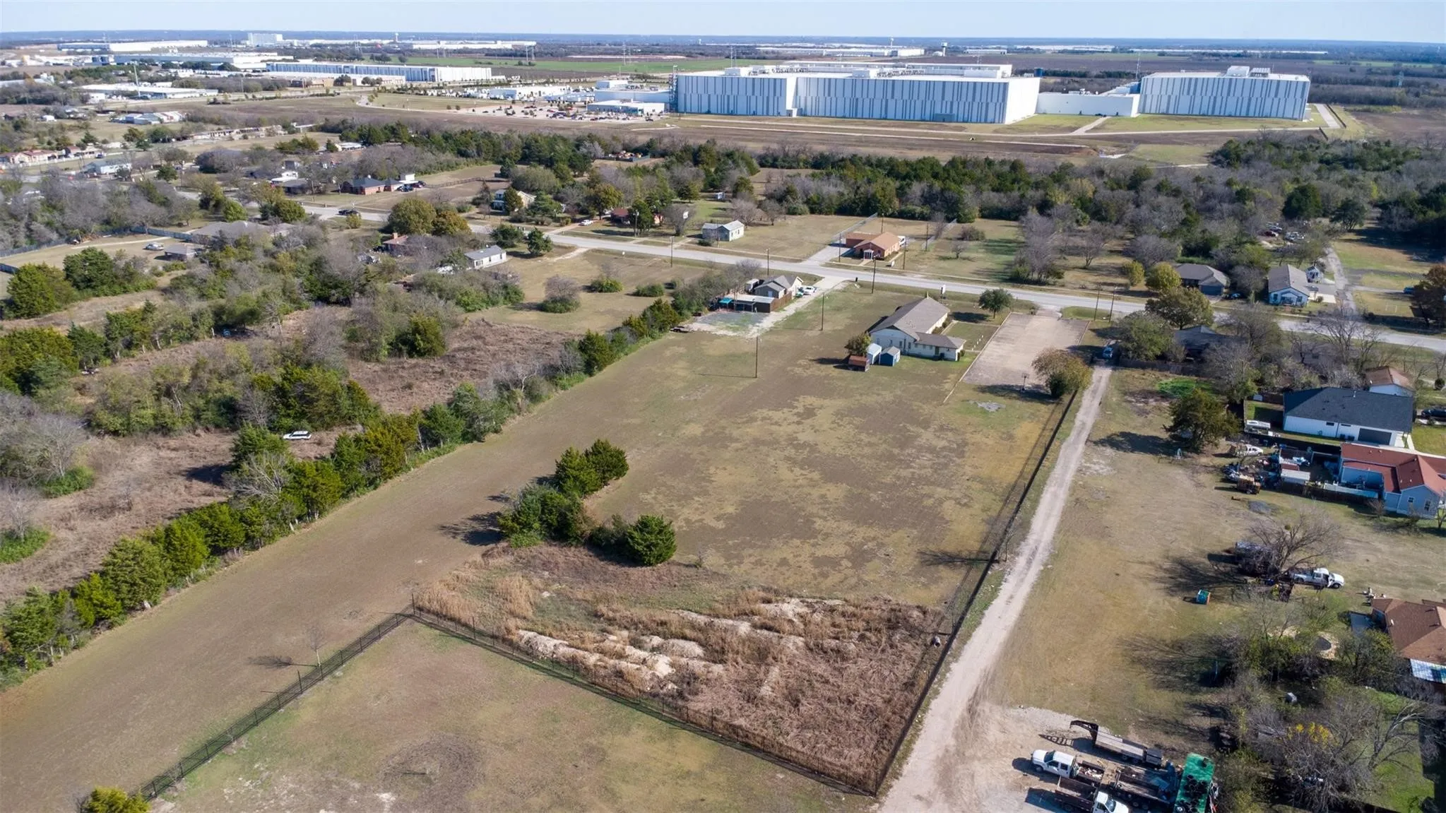 Expansive undeveloped land parcel featuring a perimeter fence, natural ground cover, scattered trees, and a gravel driveway