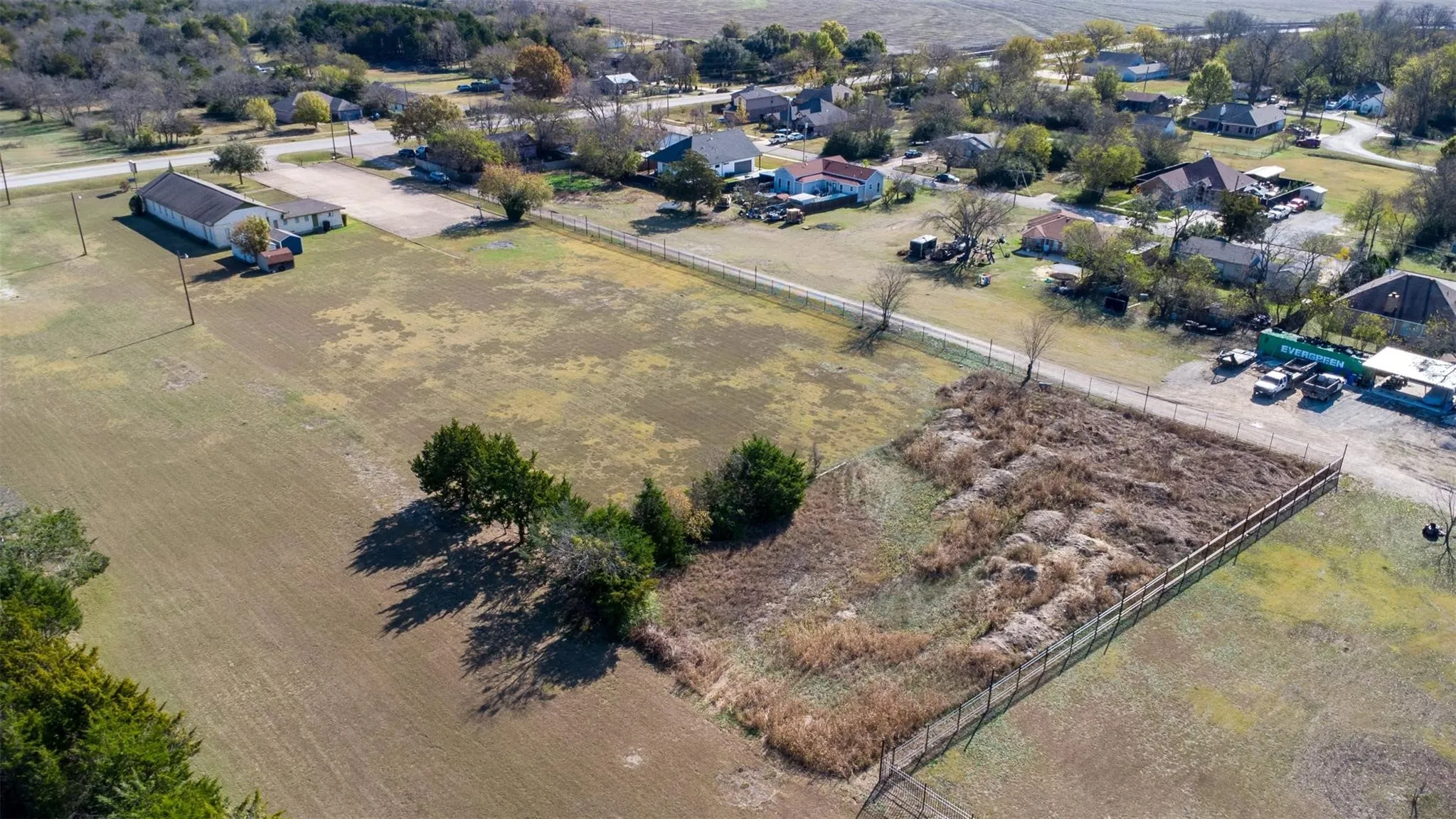 Expansive undeveloped land parcel featuring a perimeter fence and mature trees