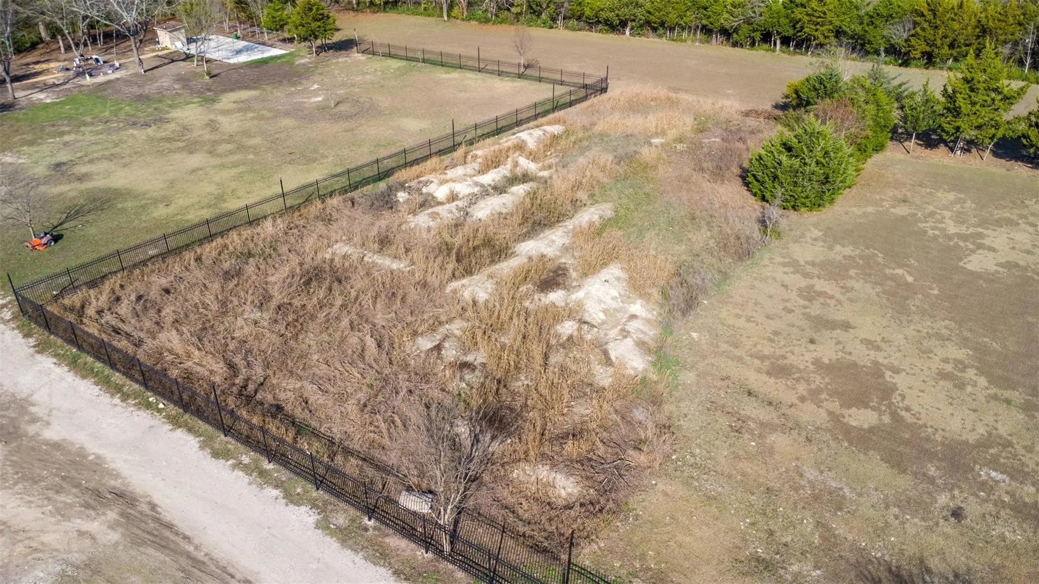 Expansive fenced lot with varied terrain, featuring open grassy areas and sections of natural vegetation