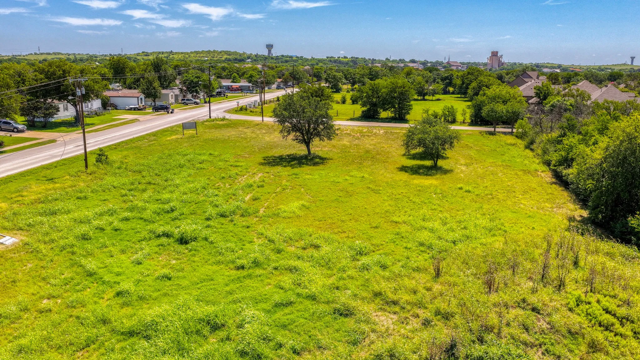 Expansive green lot featuring mature trees and a paved road frontage