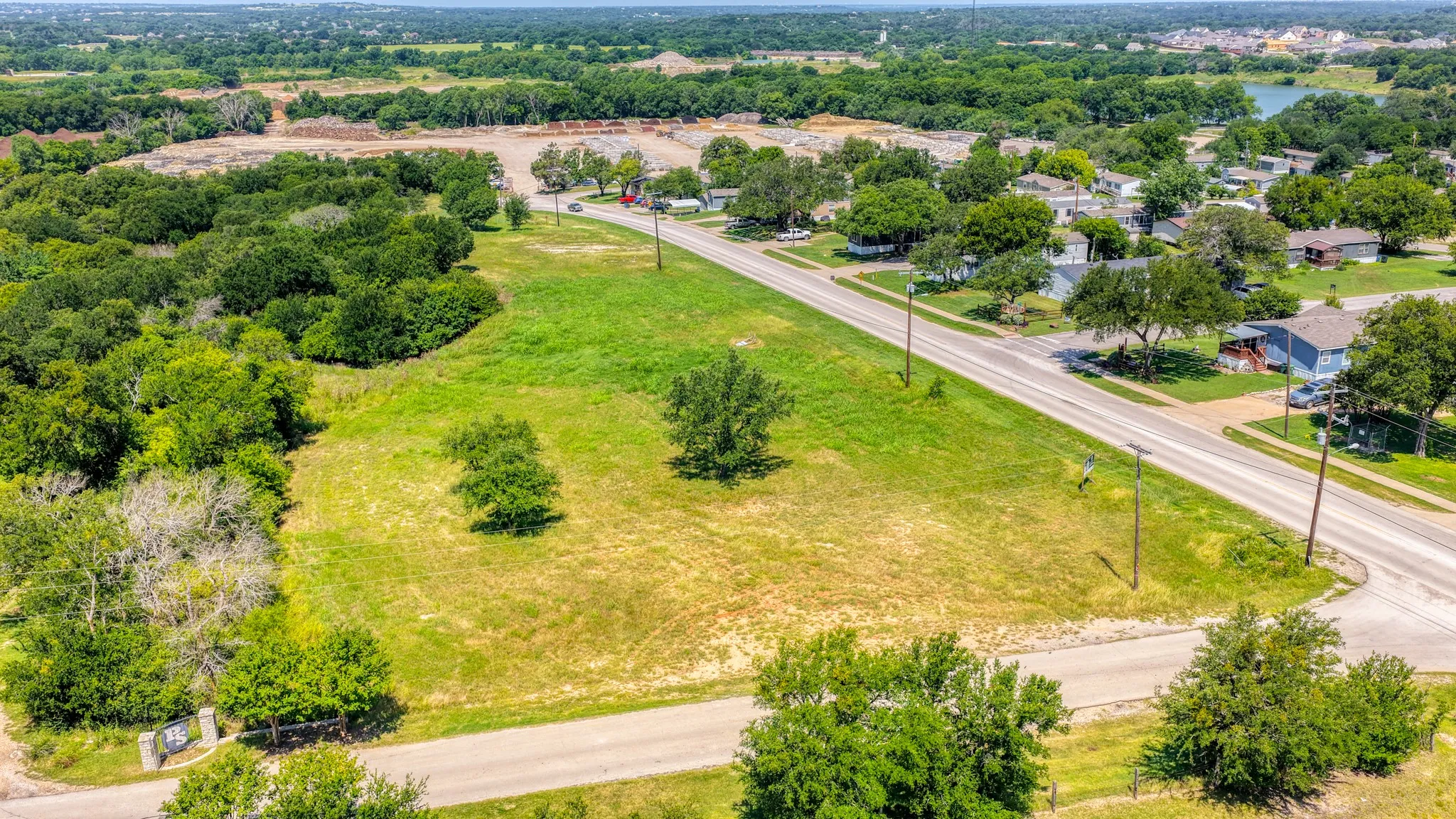 Expansive undeveloped land parcel featuring mature trees, a clear grassy area, and road frontage