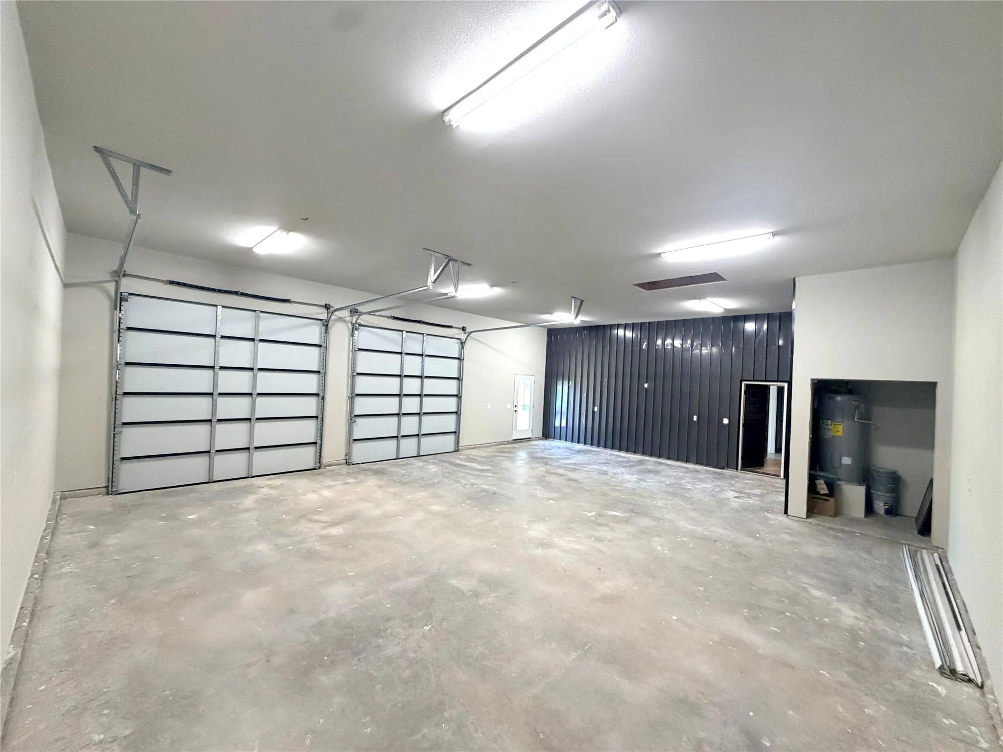 Spacious interior featuring two overhead doors, exposed concrete flooring, and a corrugated metal accent wall