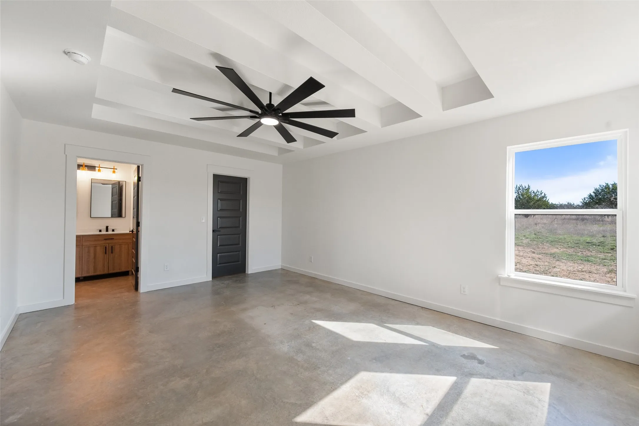 Spacious room featuring a tray ceiling with a modern ceiling fan, concrete flooring, and a large window