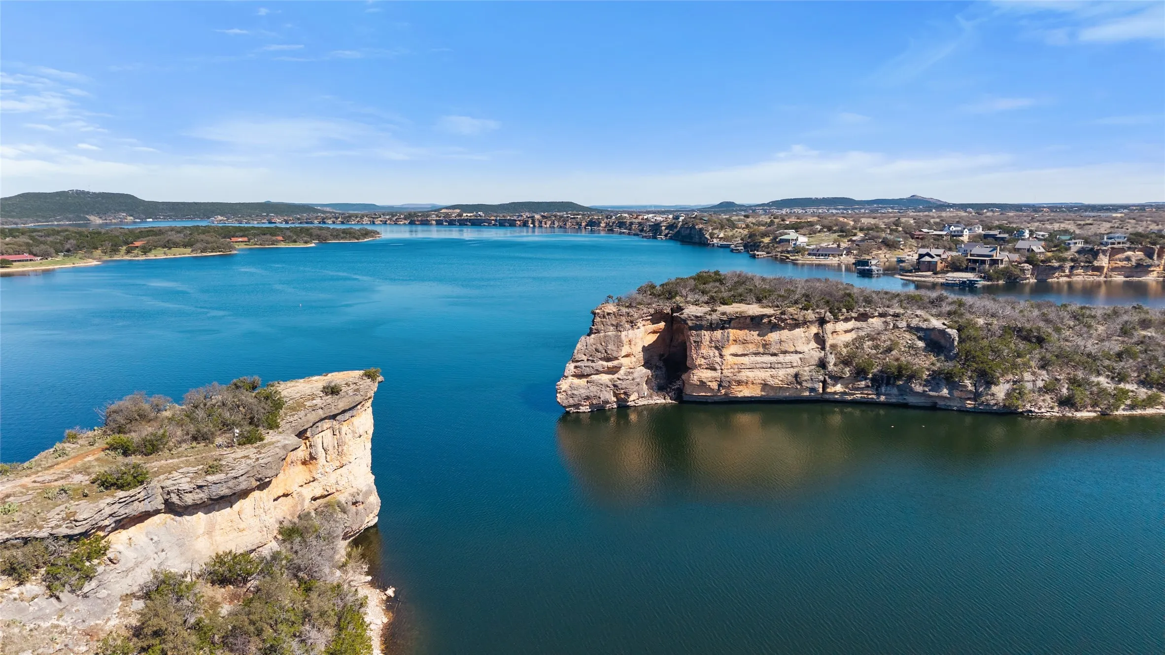 Expansive waterfront setting featuring a large body of water, rugged rock formations, and distant residential properties