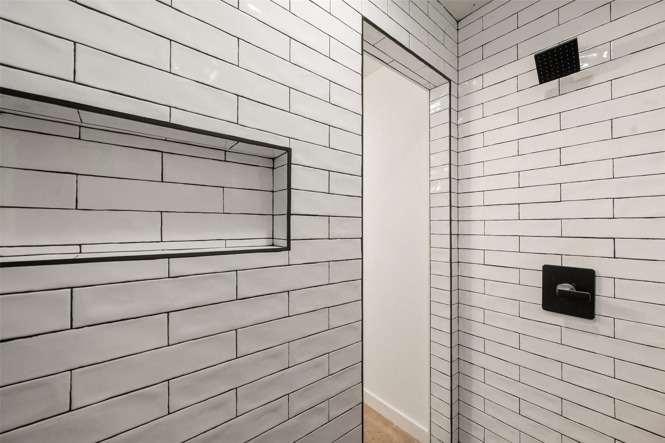 Shower stall featuring white subway tile, a built-in niche with black trim, a matte black rain shower head, and a matte black shower control