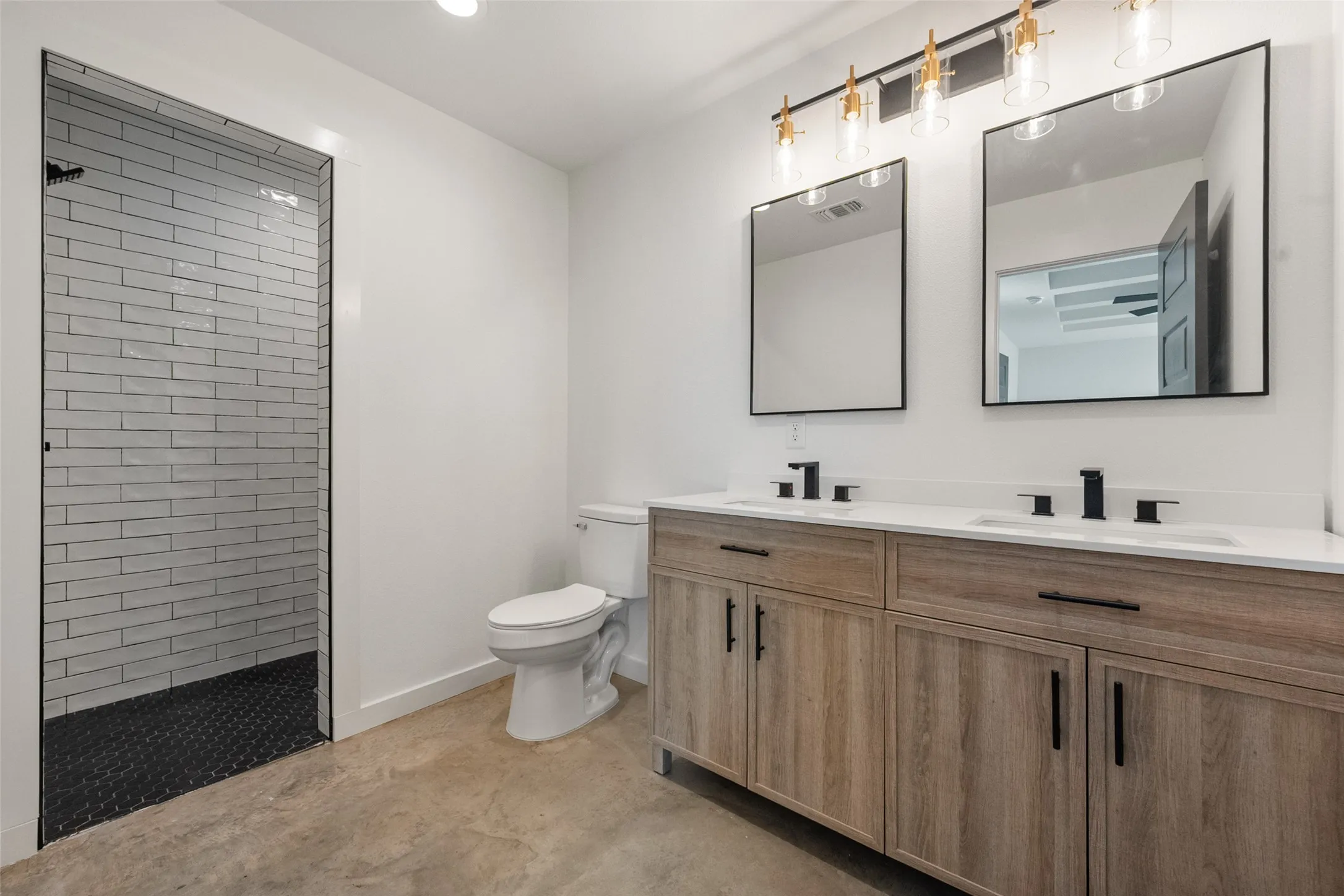 Spacious bathroom featuring a dual vanity with wood-finish cabinetry, white countertops, and matte black fixtures