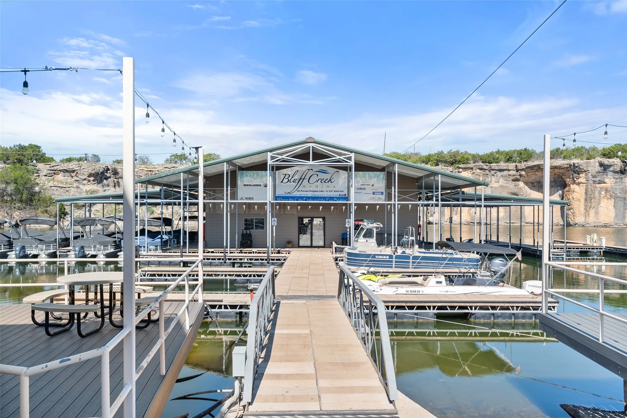 Covered marina structure featuring multiple boat slips, a central walkway, and waterfront decking with picnic tables
