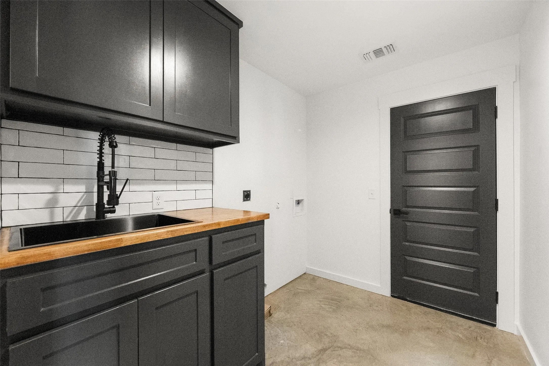 Utility area featuring dark cabinetry, a wood-finish countertop, a deep basin sink with a matte black faucet, and white subway tile backsplash