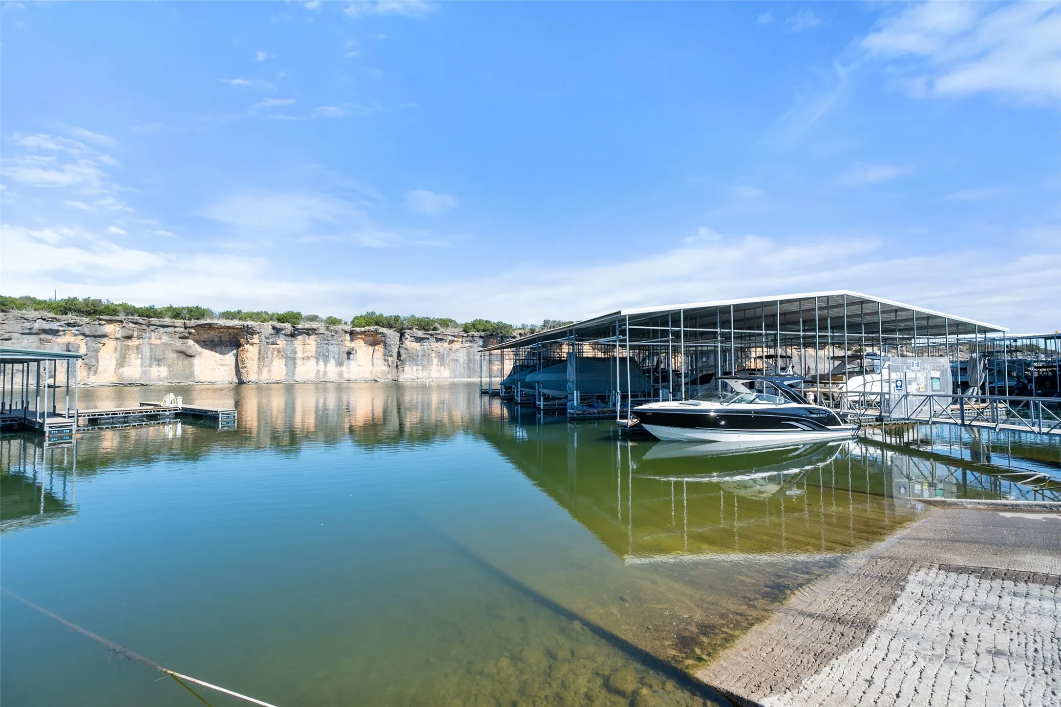 Waterfront property featuring a covered boat dock, concrete boat ramp, and multiple boat slips