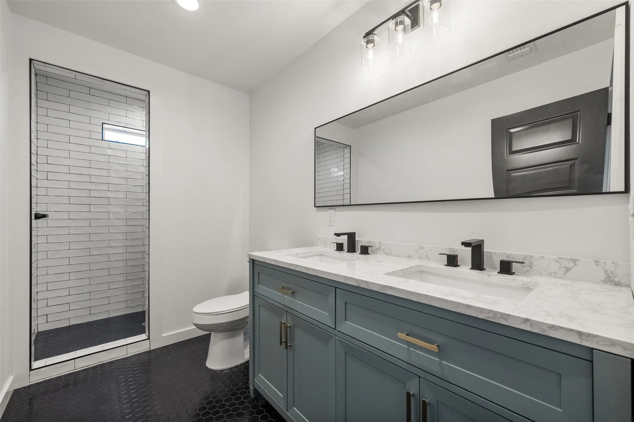 Bathroom featuring a dual vanity with a quartz countertop, matte black fixtures, and a wall-mounted mirror