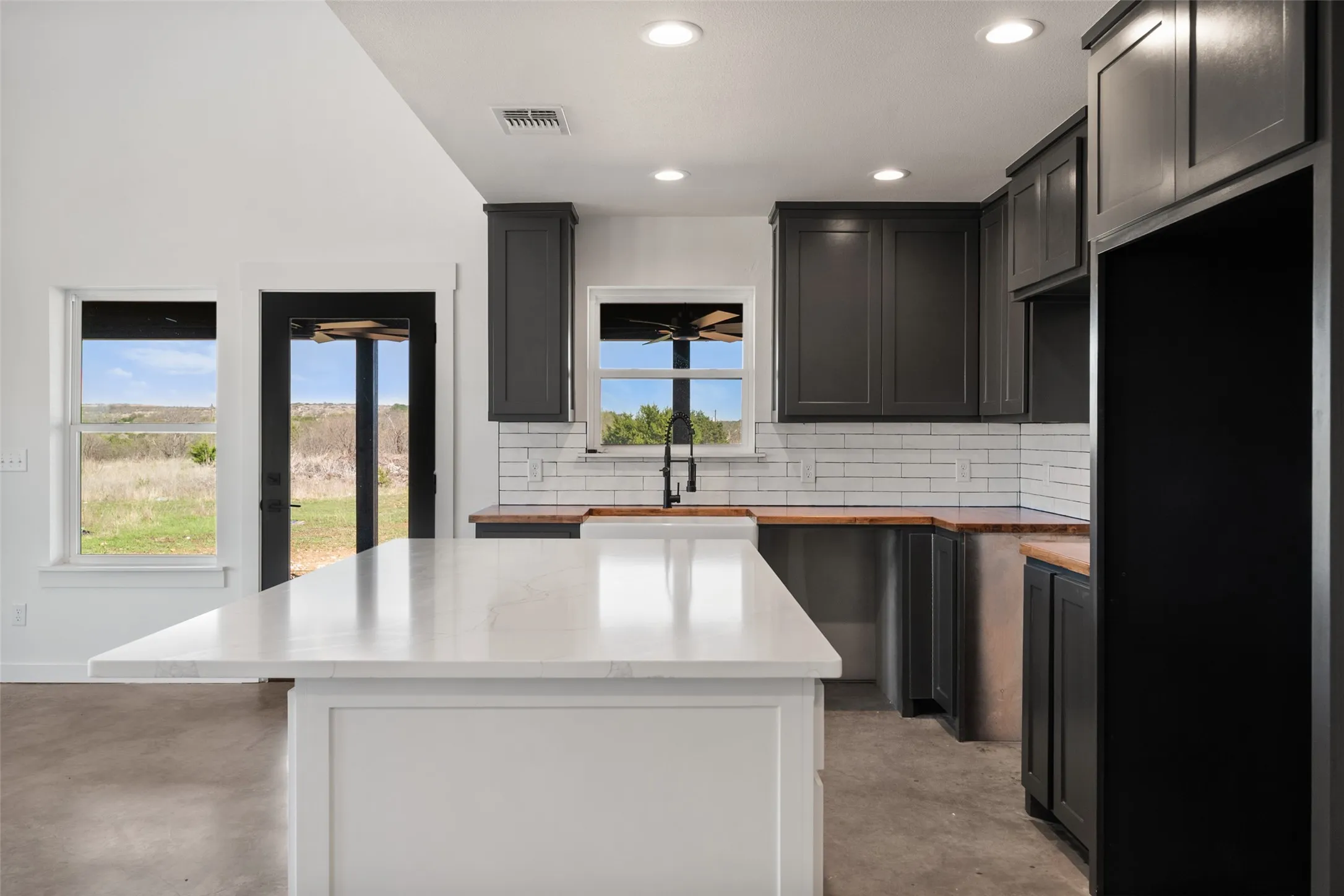 Modern kitchen featuring a white center island with a stone-finish countertop, dark gray cabinetry, wood-finish perimeter countertops, and white subway tile backsplash