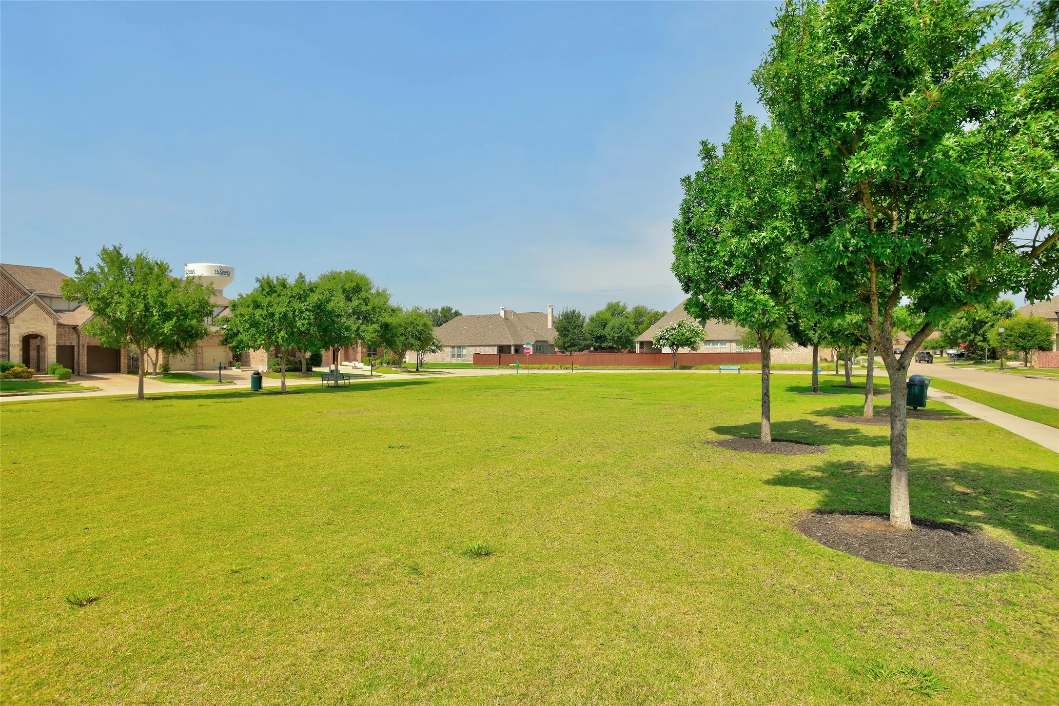 Expansive green space featuring mature trees with mulched bases and a paved pathway