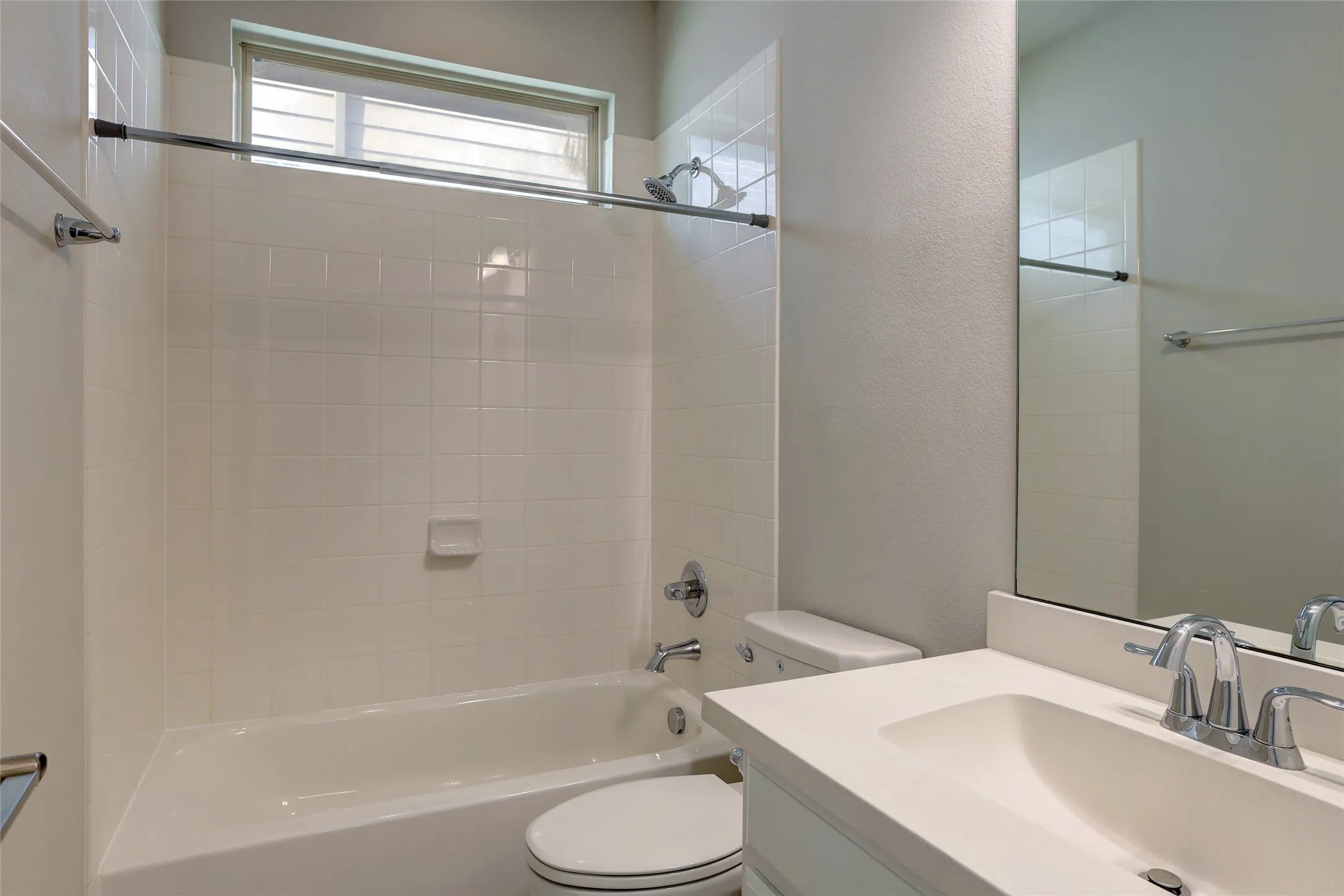 Bathroom featuring a shower/tub combination with white subway tile surround, a built-in window with horizontal blinds, a single vanity with an integrated sink and chrome faucet, and a wall-mounted mirror