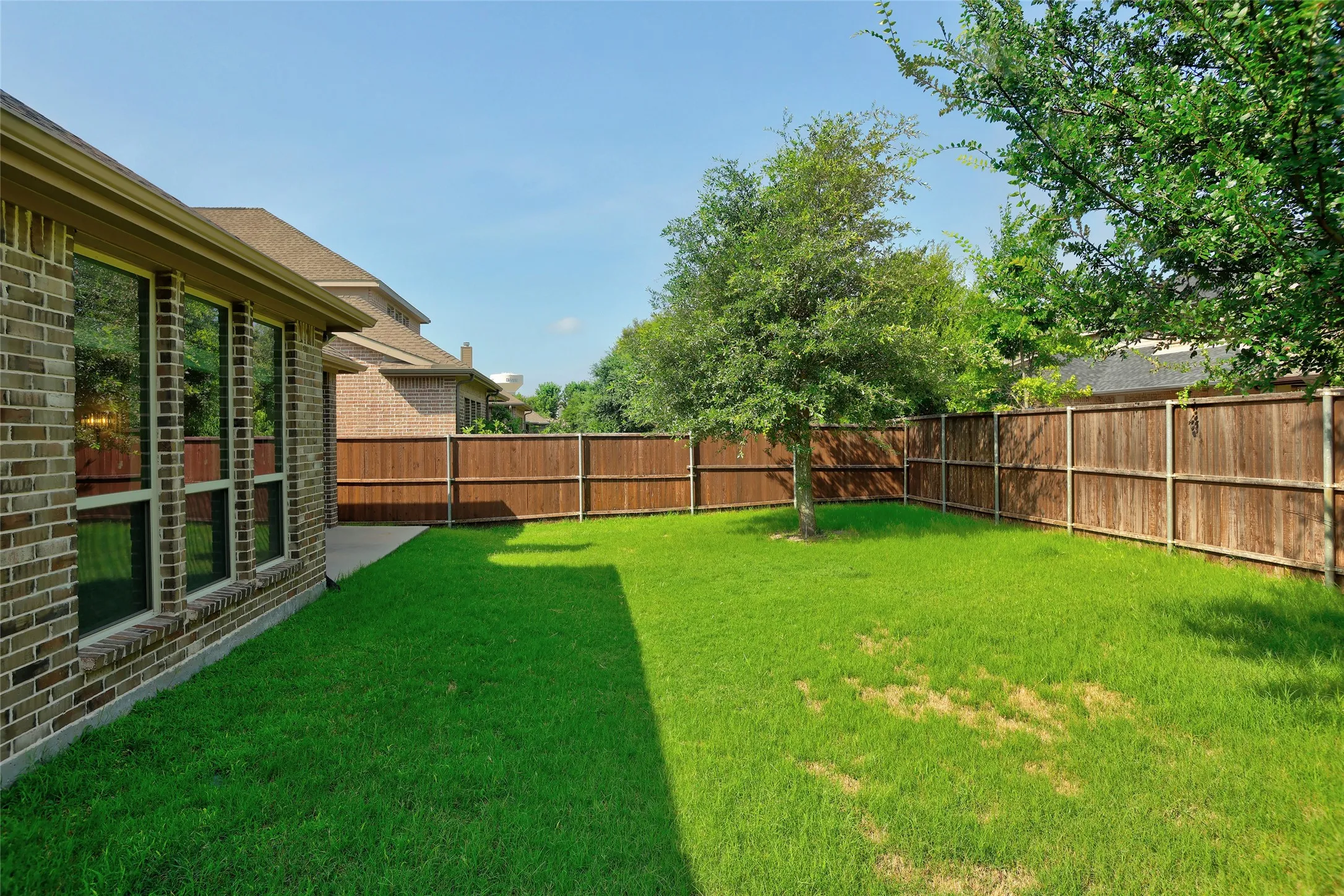 Expansive backyard featuring a manicured lawn, established tree, and full privacy fencing