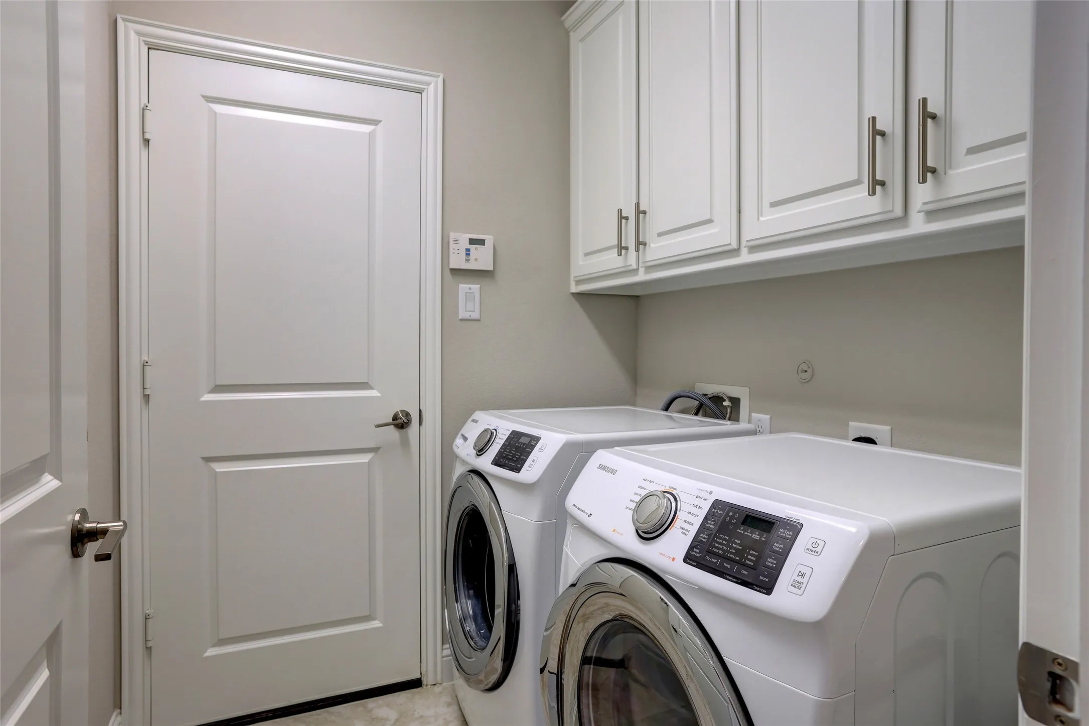 Dedicated laundry area featuring white upper cabinetry with brushed nickel hardware, light neutral wall paint, and a white paneled door