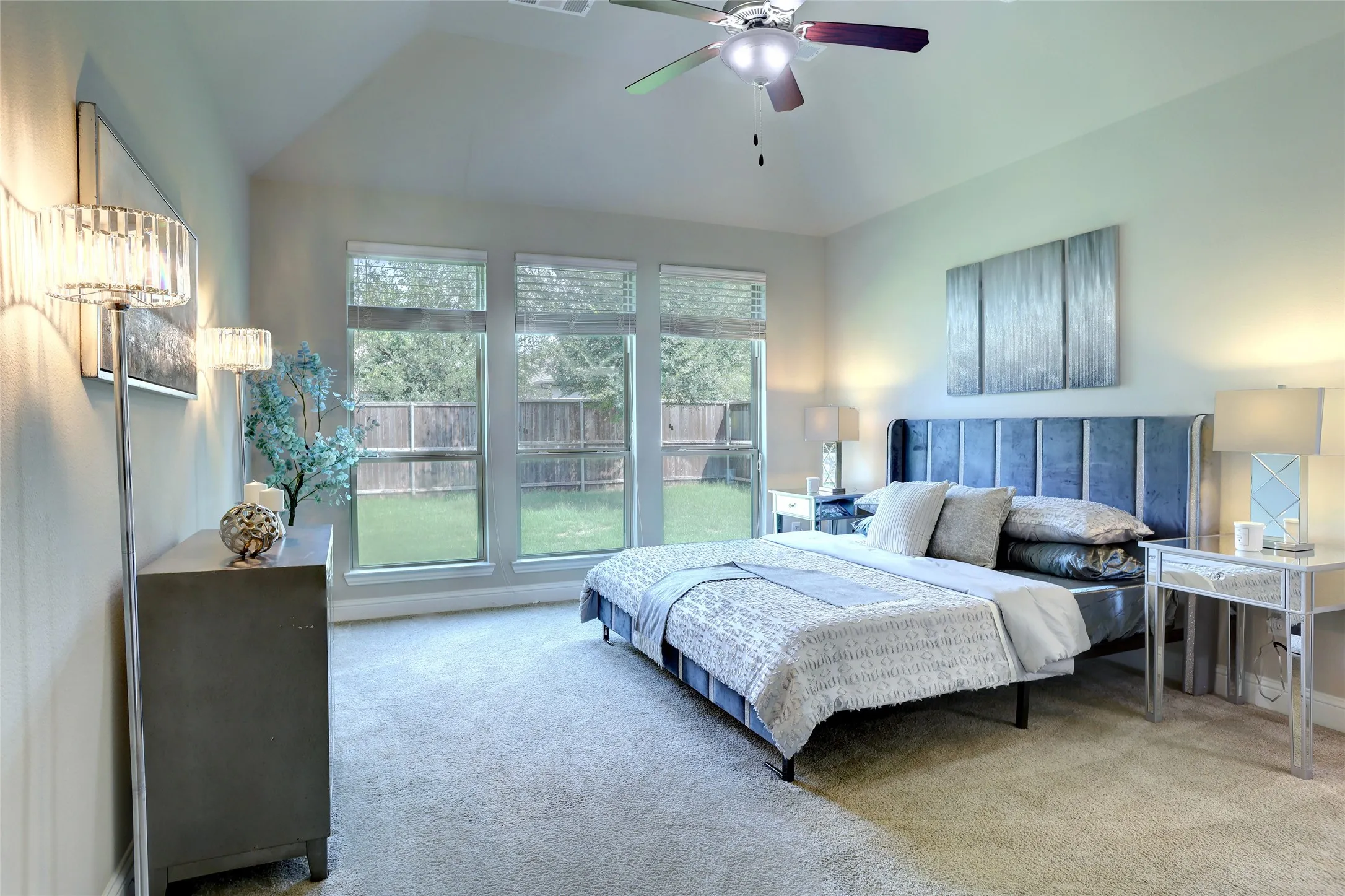 Carpeted bedroom with a vaulted ceiling, ceiling fan, and three large windows