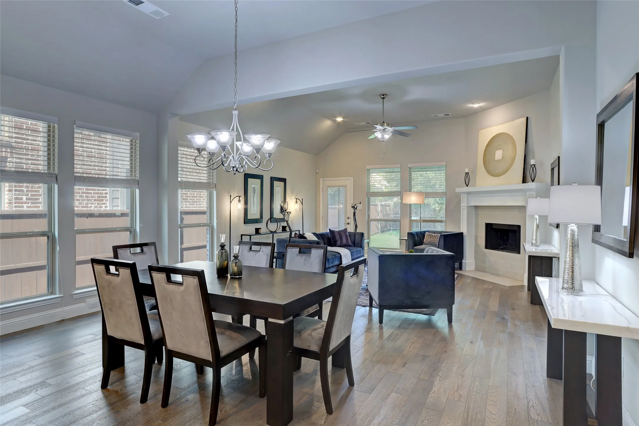 Open-concept living and dining areas featuring wood-finish flooring, vaulted ceilings, a built-in fireplace with mantle, and multiple windows