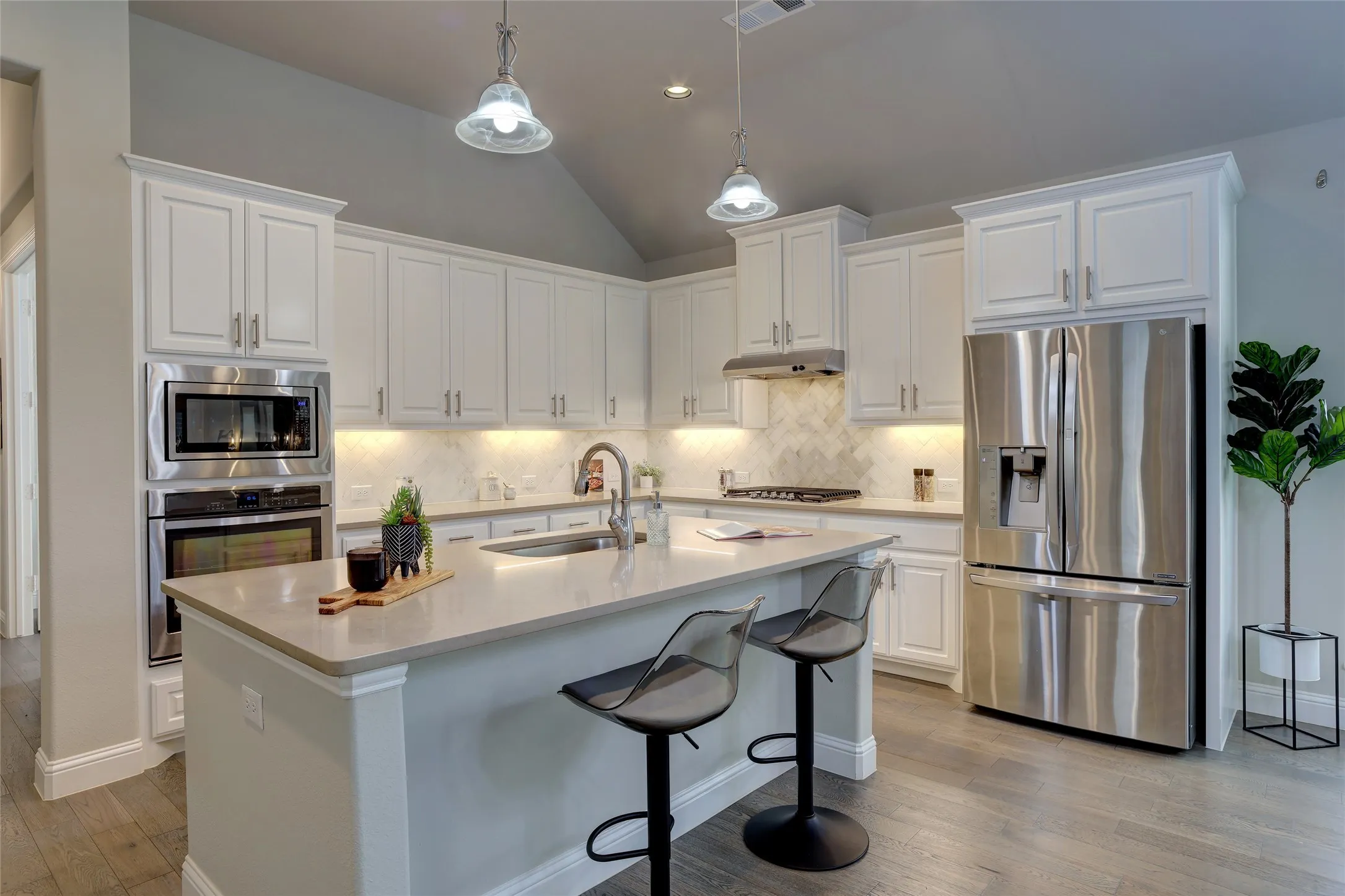 Kitchen featuring white cabinetry with under-cabinet lighting, a central island with countertop seating, stainless steel appliances, and wood-finish flooring