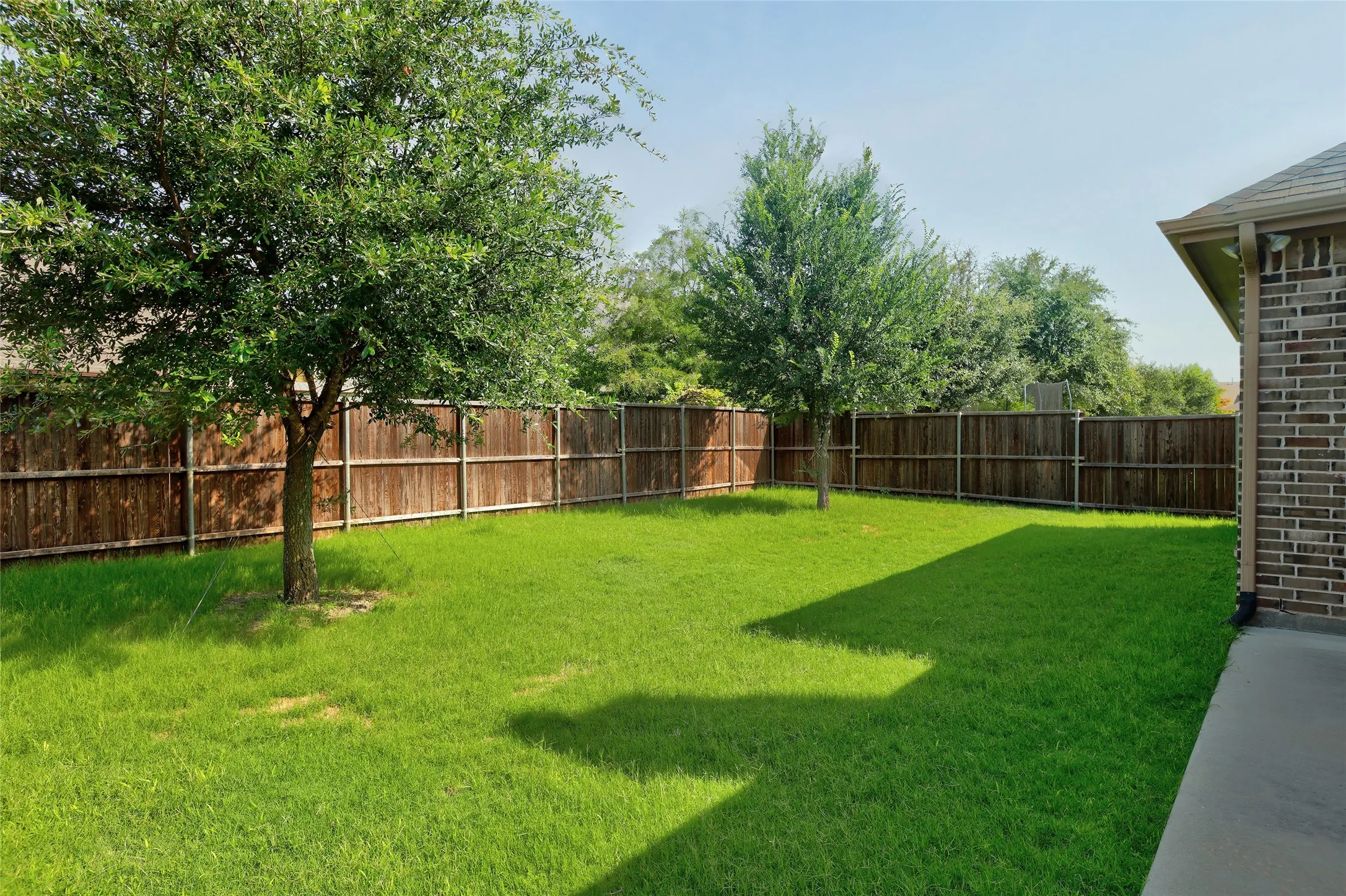Expansive backyard featuring a lush green lawn, two mature trees, privacy fencing, and a concrete patio space